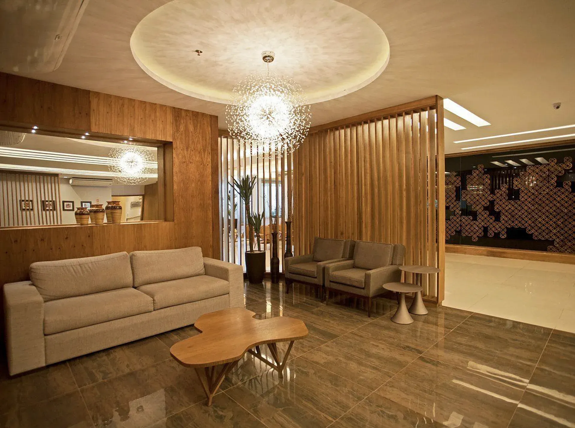 Lobby de hotel moderno com sofás bege, ripas de madeira, piso de mármore e luminárias pendentes.