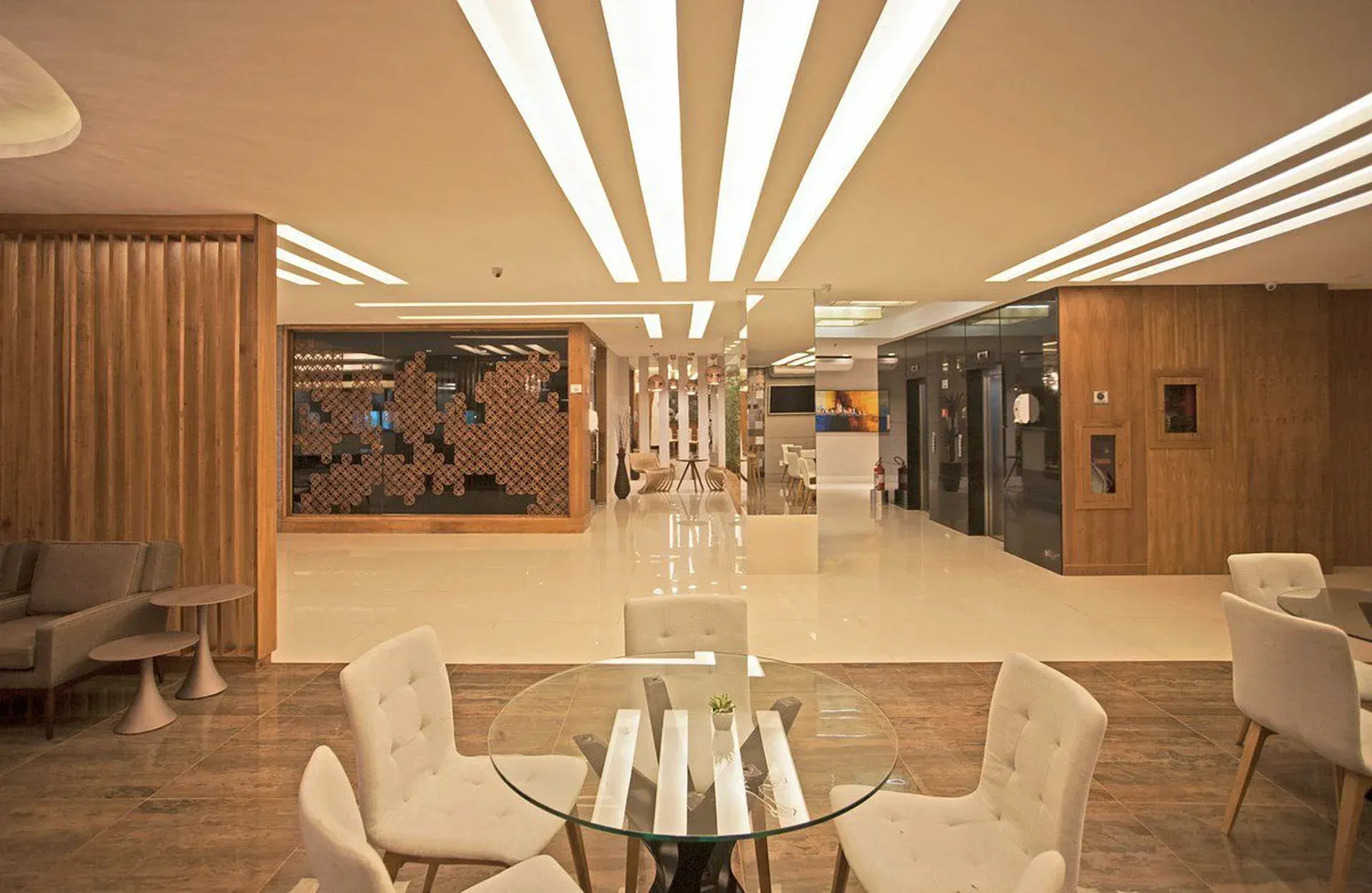 Lobby de hotel moderno com painéis de madeira em tons quentes, sofás e luminárias lineares de teto com iluminação intensa.
