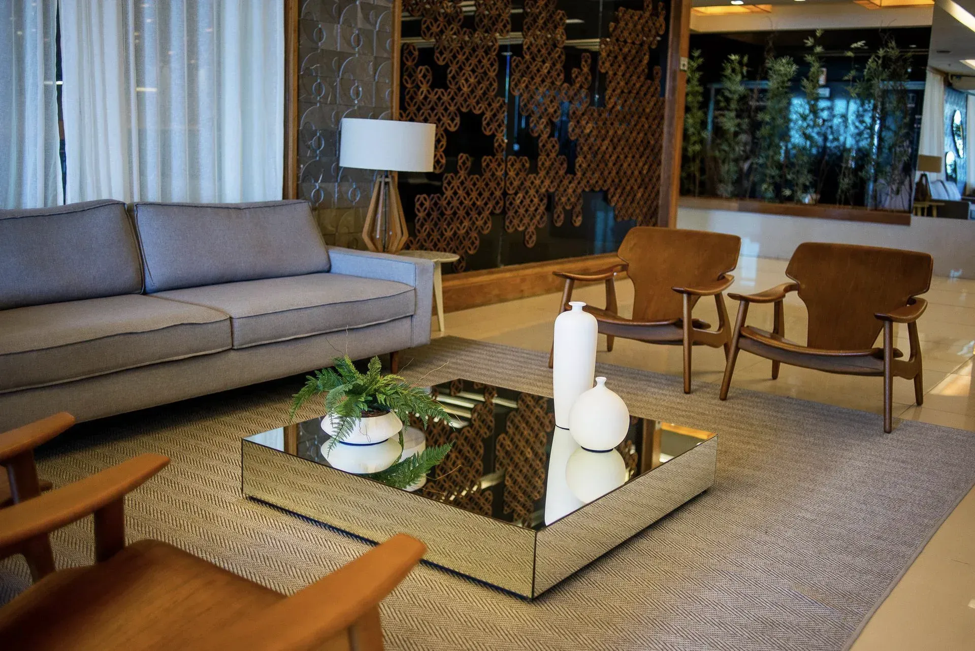 Sala de estar moderna com sofá bege, cadeiras de madeira, mesa de centro de vidro e decoração neutra.