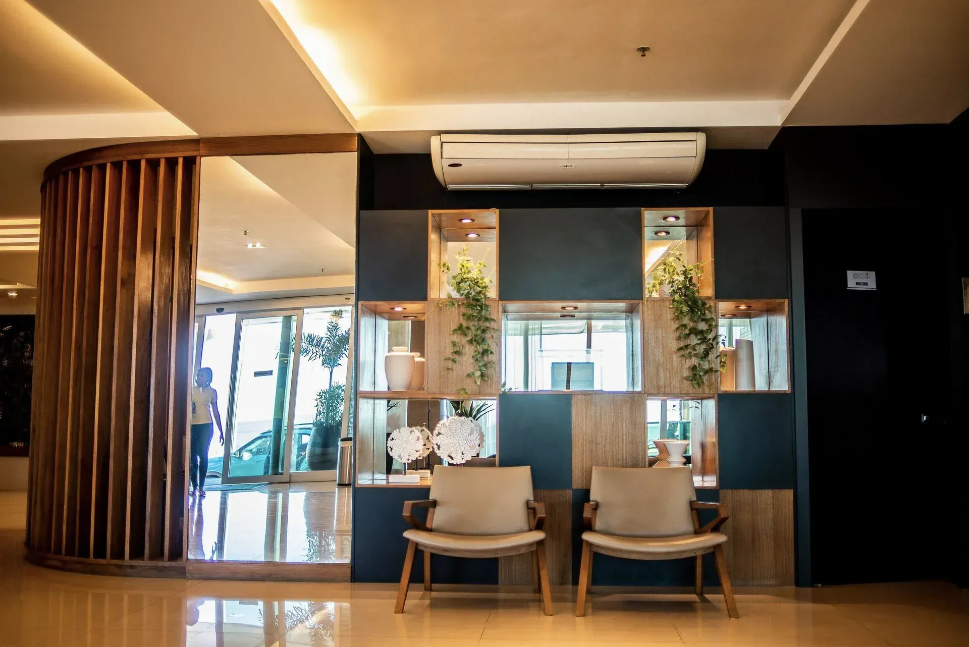 Hall de entrada moderno do hotel com poltronas, balcão de recepção com painéis de madeira e janelas do chão ao teto.