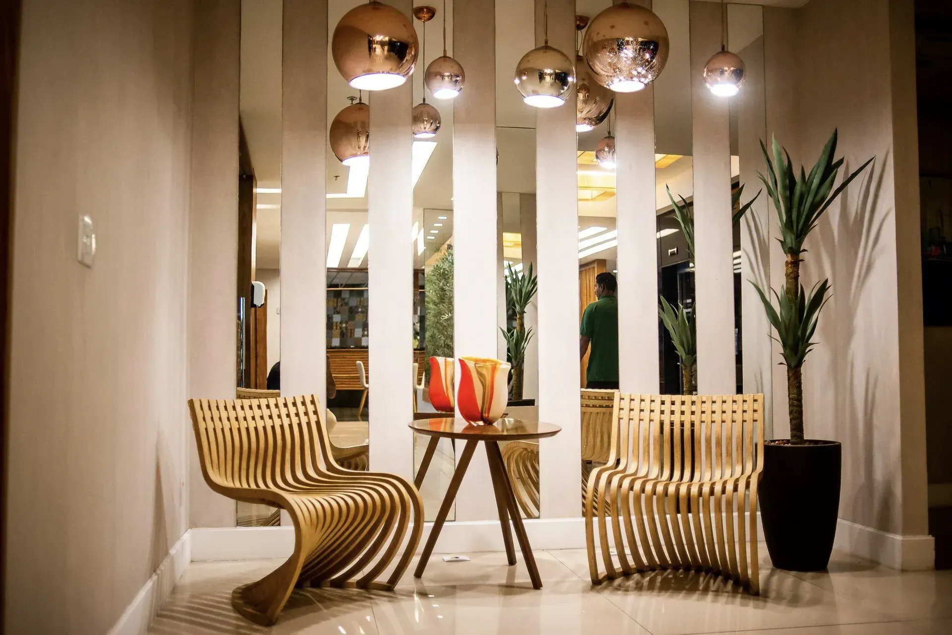Hall de entrada moderno com cadeiras esculturais de madeira, luminárias pendentes e altas colunas brancas.