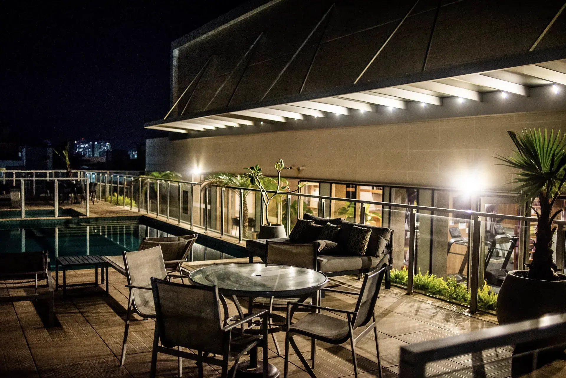 Terraço ao ar livre na cobertura à noite, com mesas, cadeiras, iluminação aconchegante e vista para a cidade.
