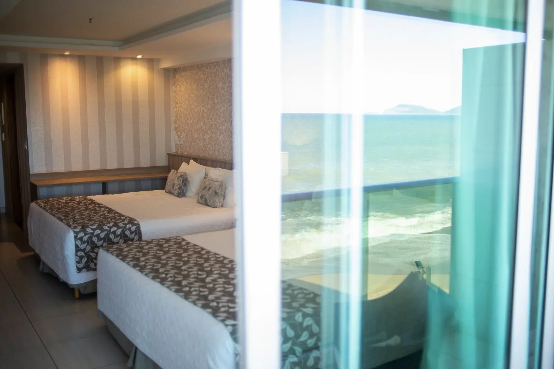 Quarto de hotel com duas camas de solteiro ao lado de uma grande janela com vista para o oceano.