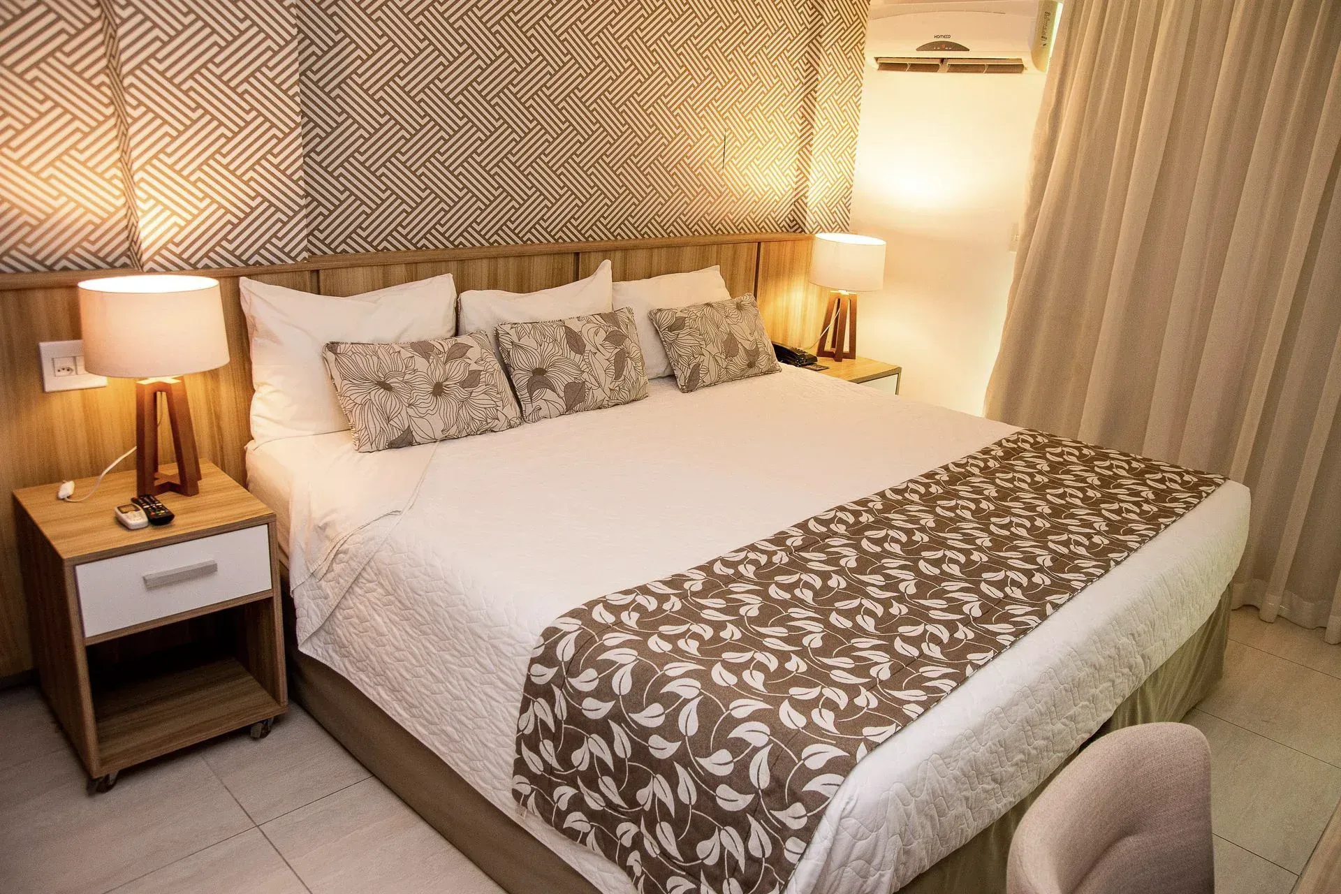 Quarto aconchegante com uma cama grande, abajures, decoração de parede em tecido e tons neutros suaves.