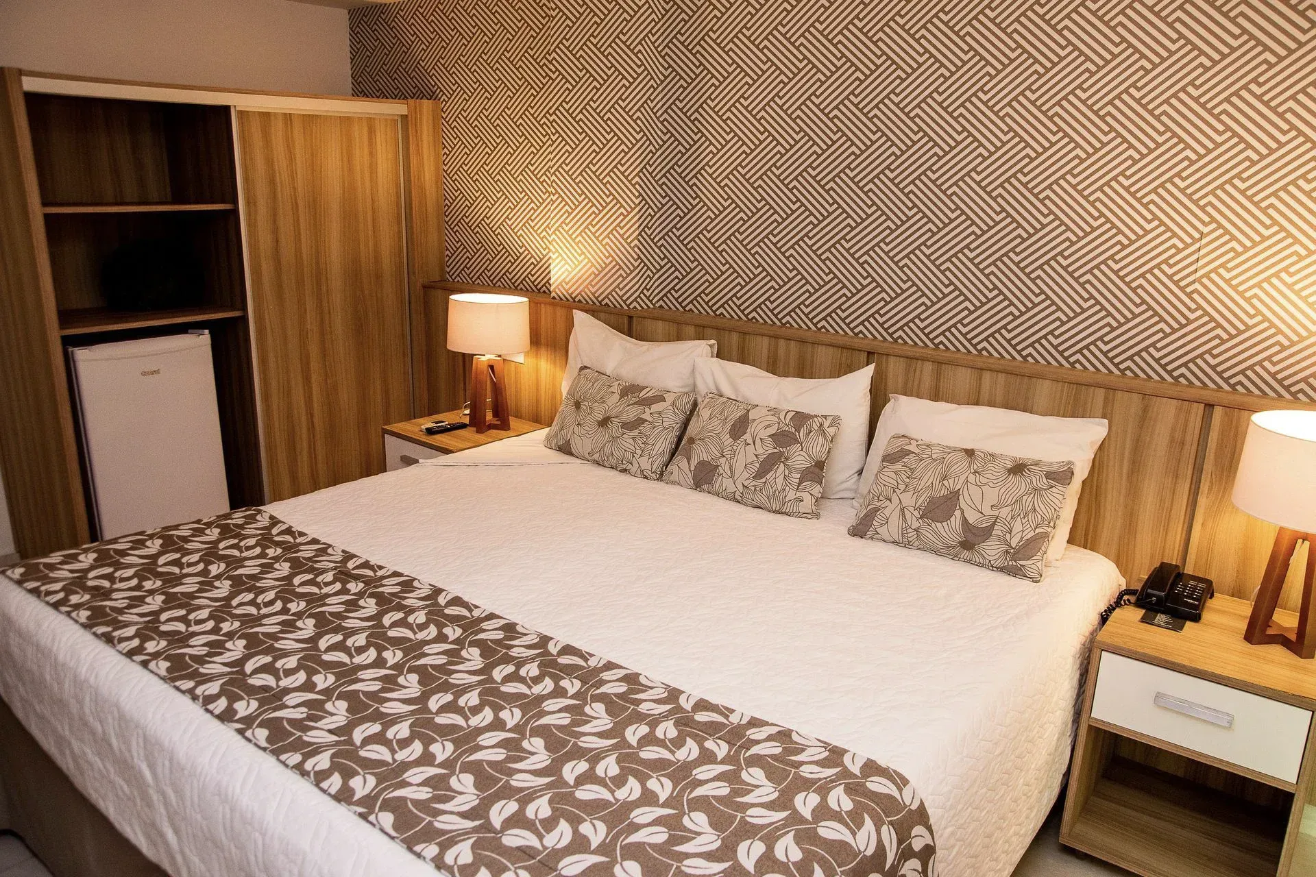 Quarto de hotel aconchegante com cama de casal, decoração estampada, abajures e guarda-roupa aberto.