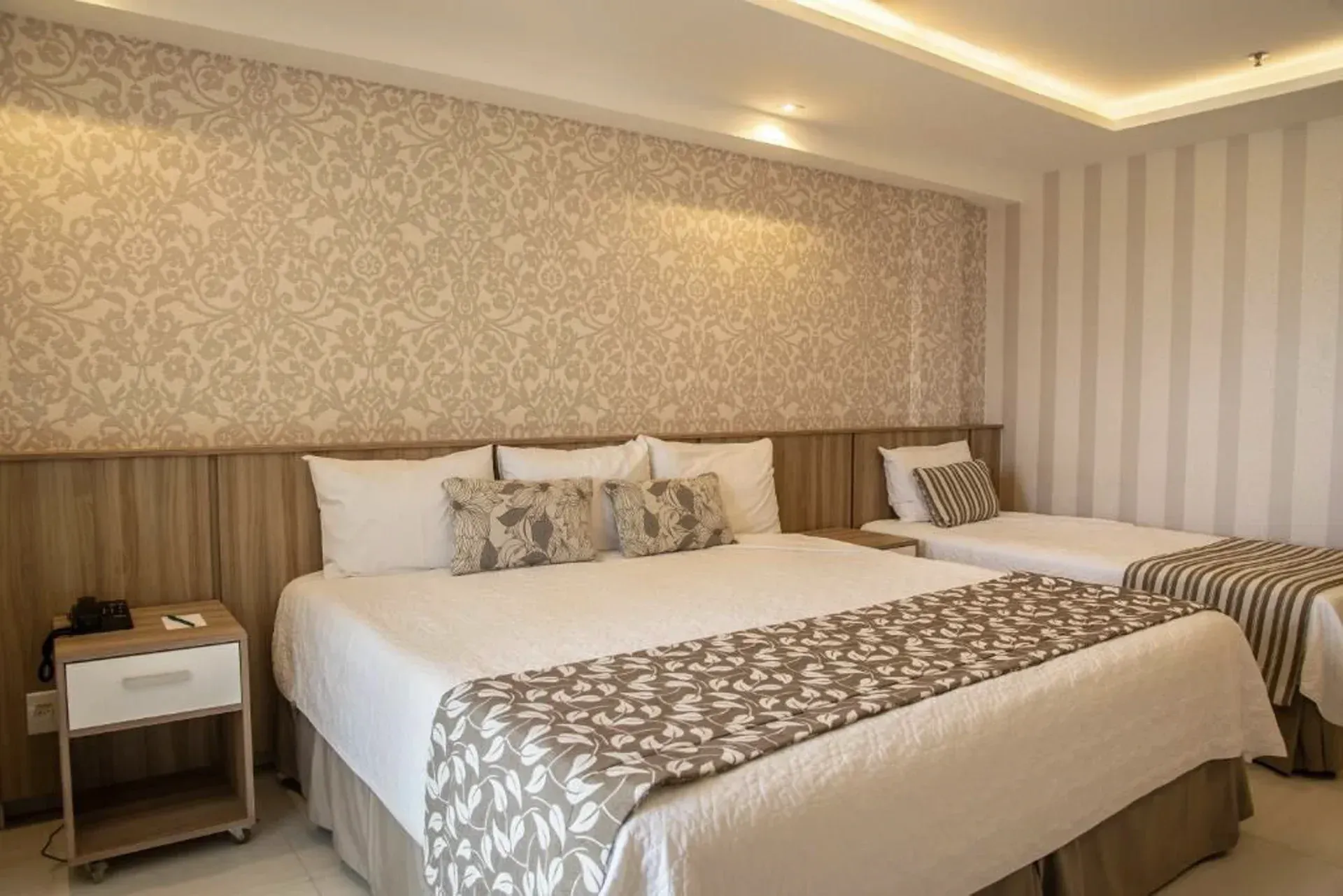 Quarto de hotel moderno com duas camas de casal, papel de parede estampado e iluminação suave e aconchegante.