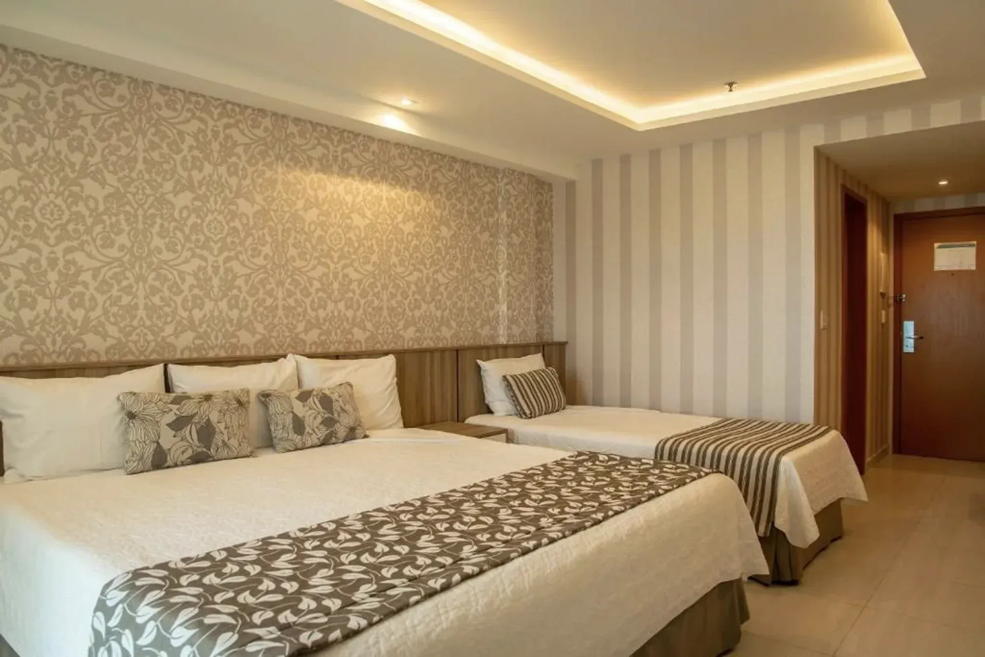 Quarto de hotel moderno com duas camas de solteiro bem arrumadas, papel de parede estampado e iluminação aconchegante.
