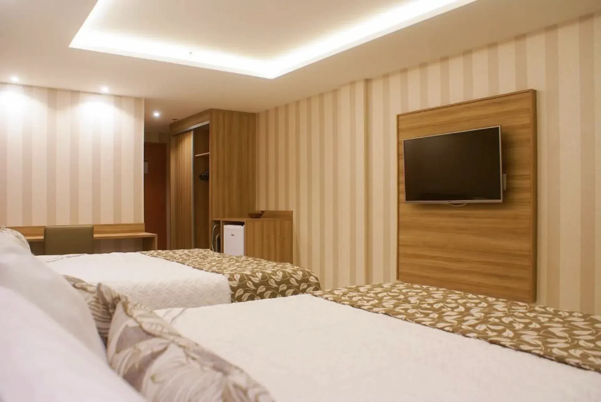 Quarto de hotel com duas camas, papel de parede listrado, parede da TV com painéis de madeira e iluminação aconchegante.