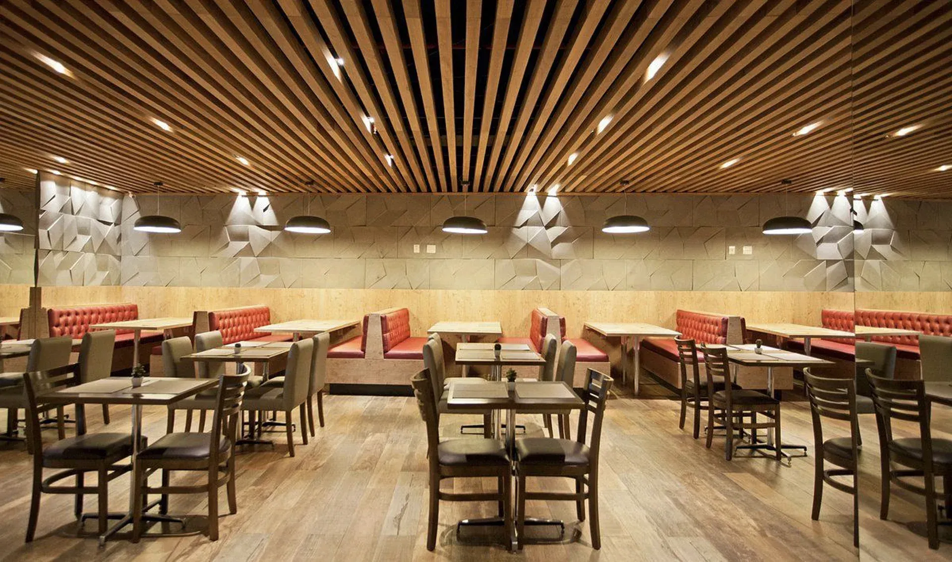 Sala de jantar vazia de um restaurante moderno com mesas e cadeiras de madeira, bancos vermelhos e teto de madeira.