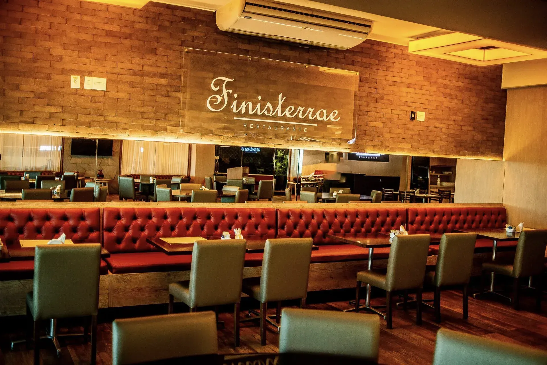 Interior de restaurante vazio com parede de tijolos, cabines vermelhas e um espelho atrás do bar.