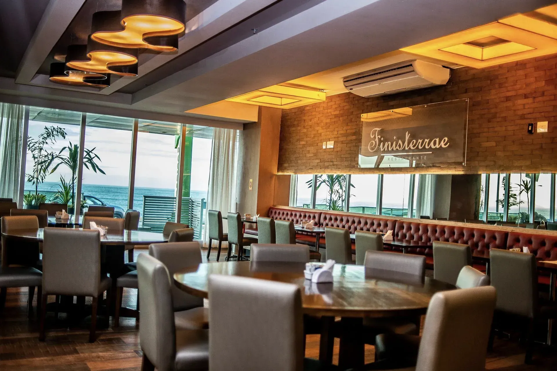 Sala de jantar elegante do restaurante com poltronas de couro, iluminação aconchegante e vista para o mar.