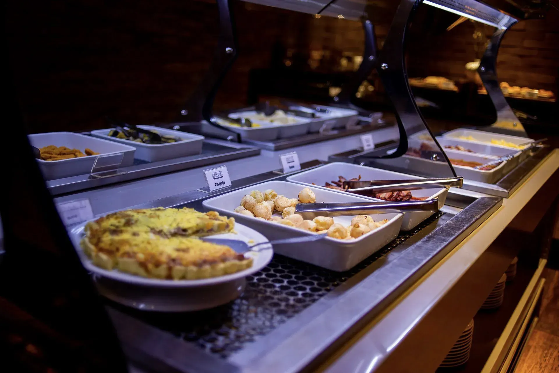 Balcão de buffet com bandejas de comida sob lâmpadas de aquecimento em um restaurante ou refeitório.