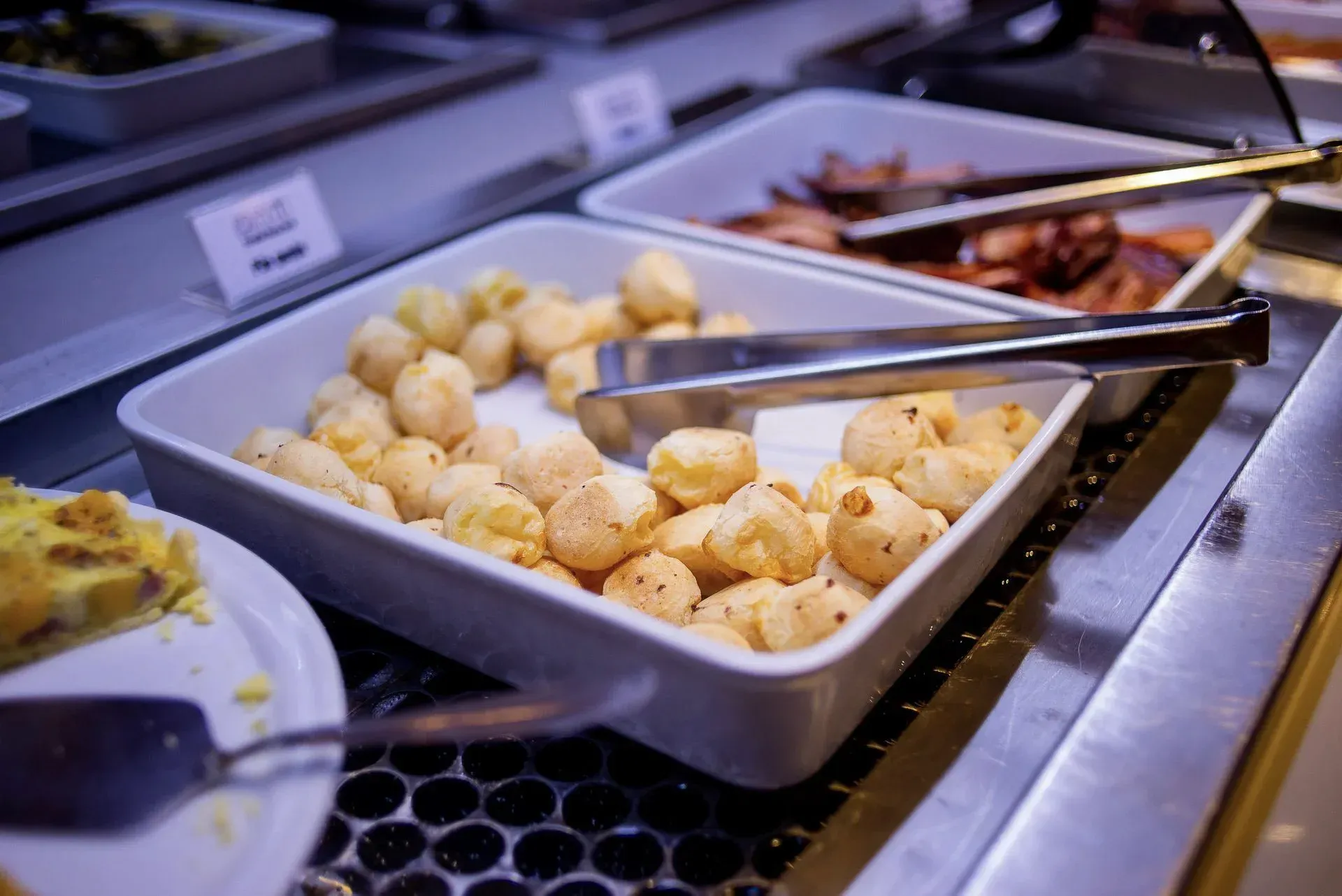 Bandeja de batatas assadas em um buffet, com pegadores e outros pratos por perto.