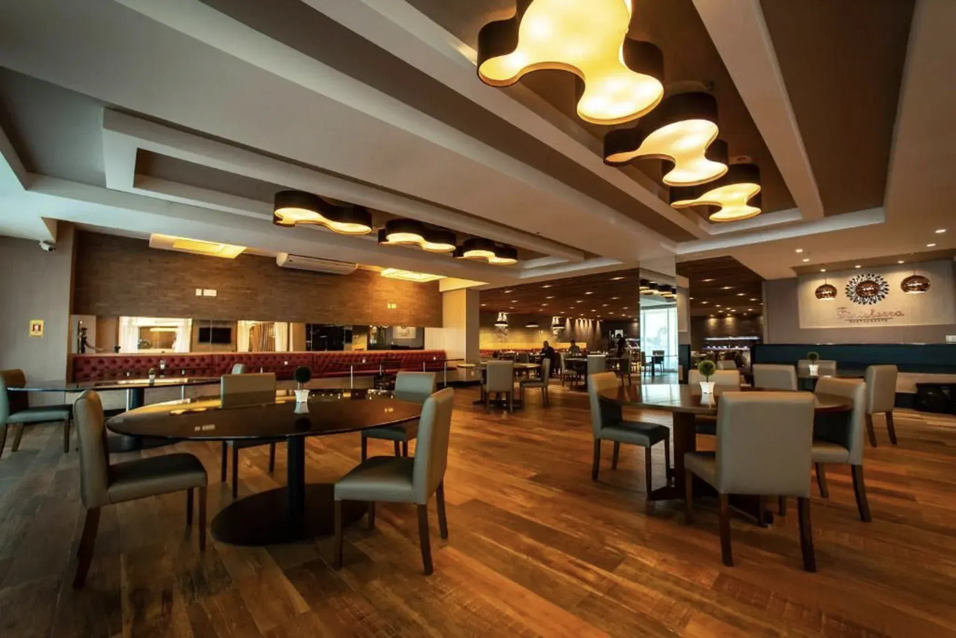 Interior espaçoso e moderno de restaurante com piso de madeira, luminárias pendentes e mesas e cadeiras dispostas com esmero.