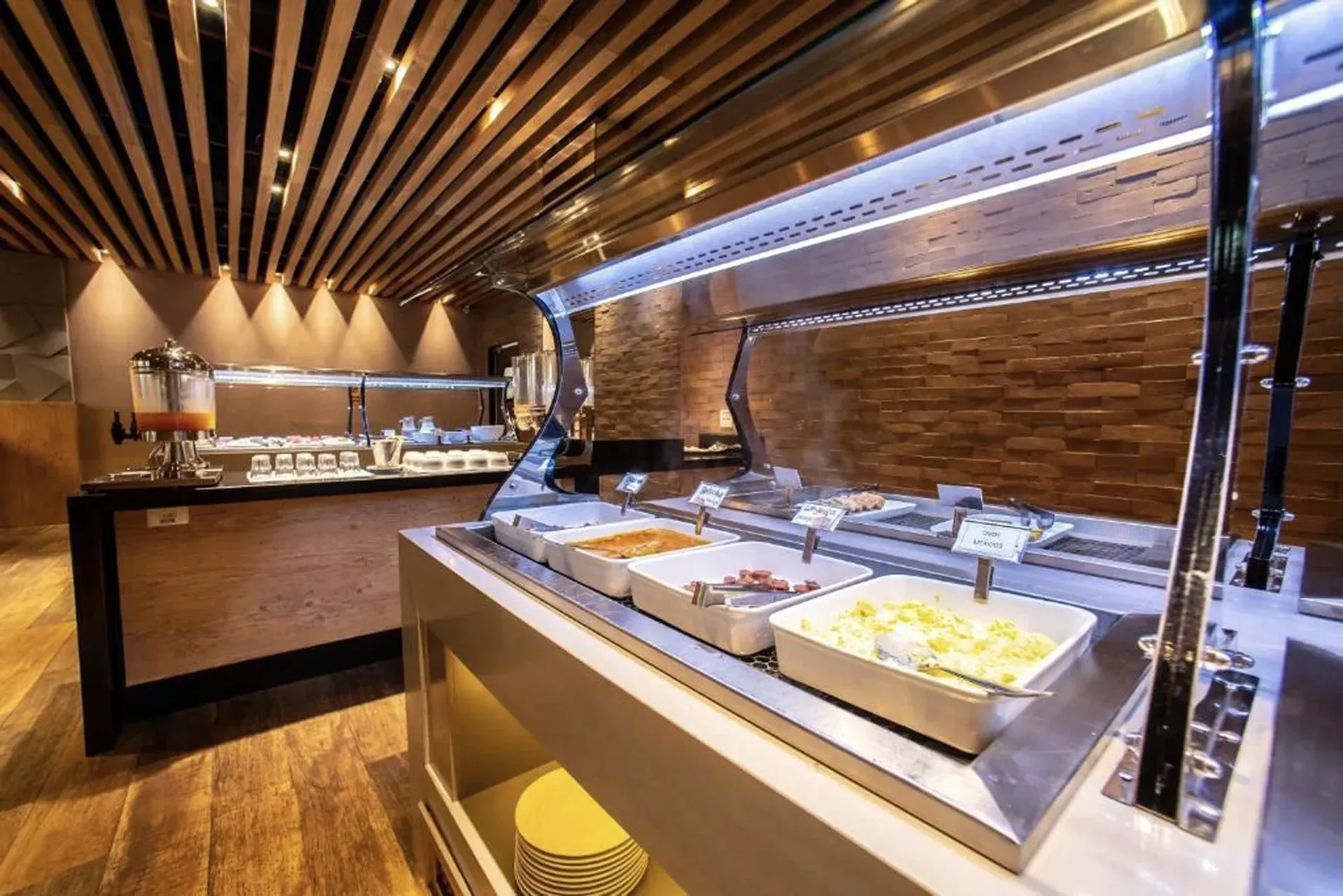 Balcão de buffet em um restaurante moderno com bandejas de comida sob iluminação aconchegante de madeira.