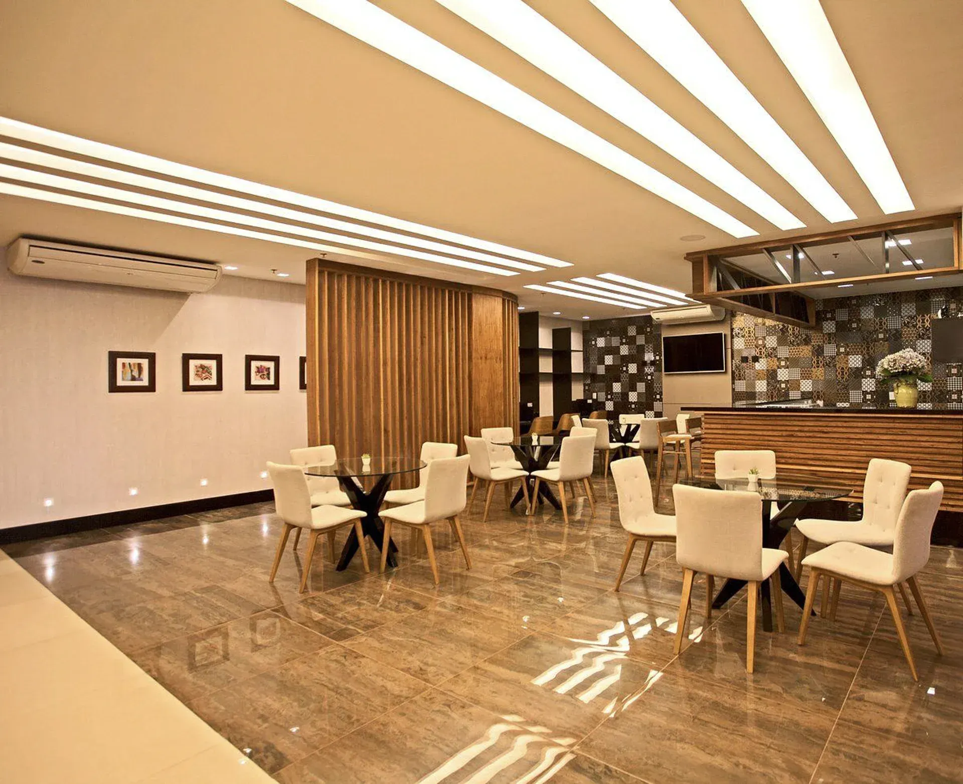 Sala de estar moderna do hotel com cadeiras cor creme, mesas de mármore, iluminação aconchegante e piso polido.