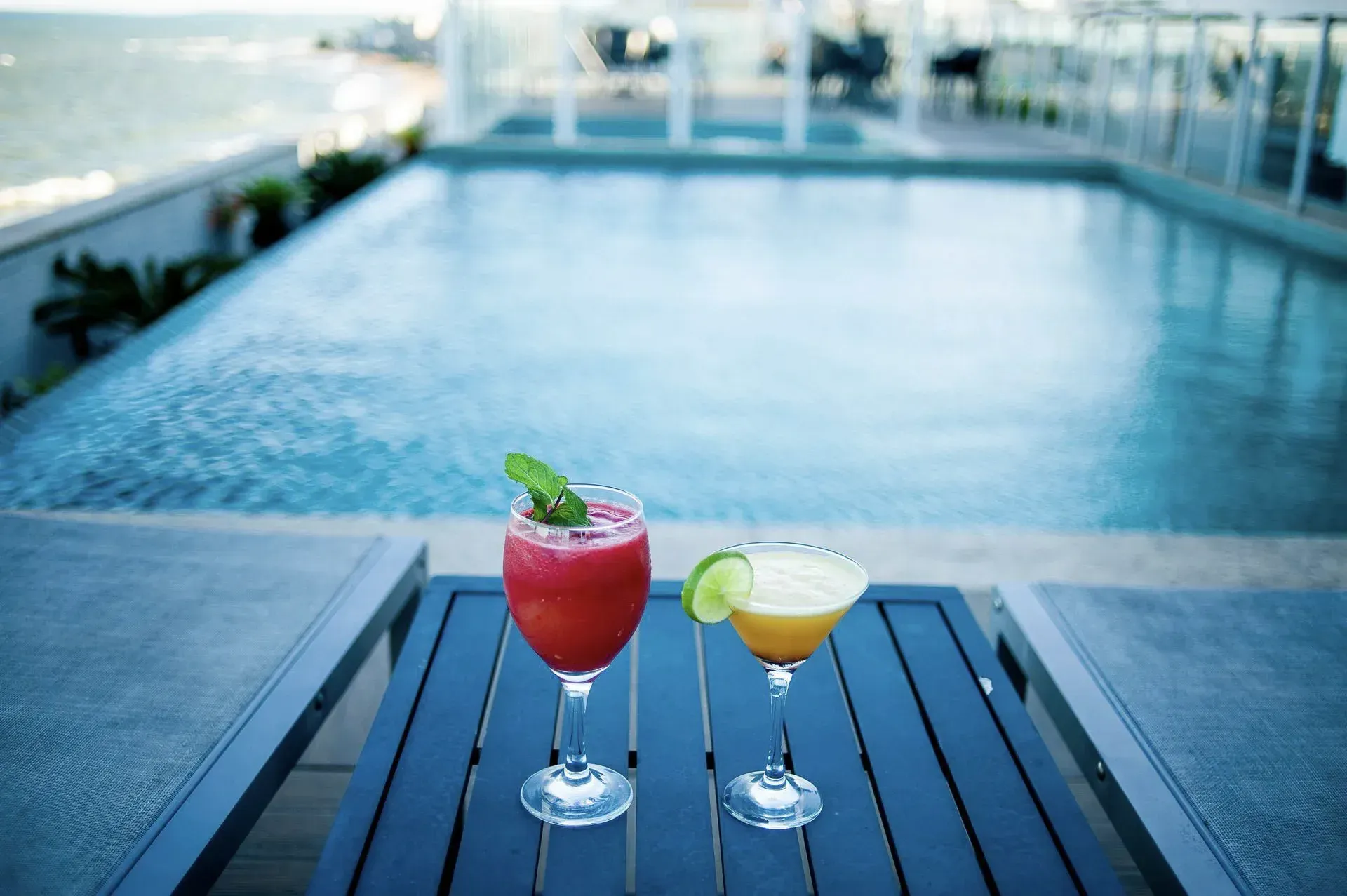 Dois coquetéis coloridos sobre uma mesa ao lado de uma piscina infinita com vista para a água.