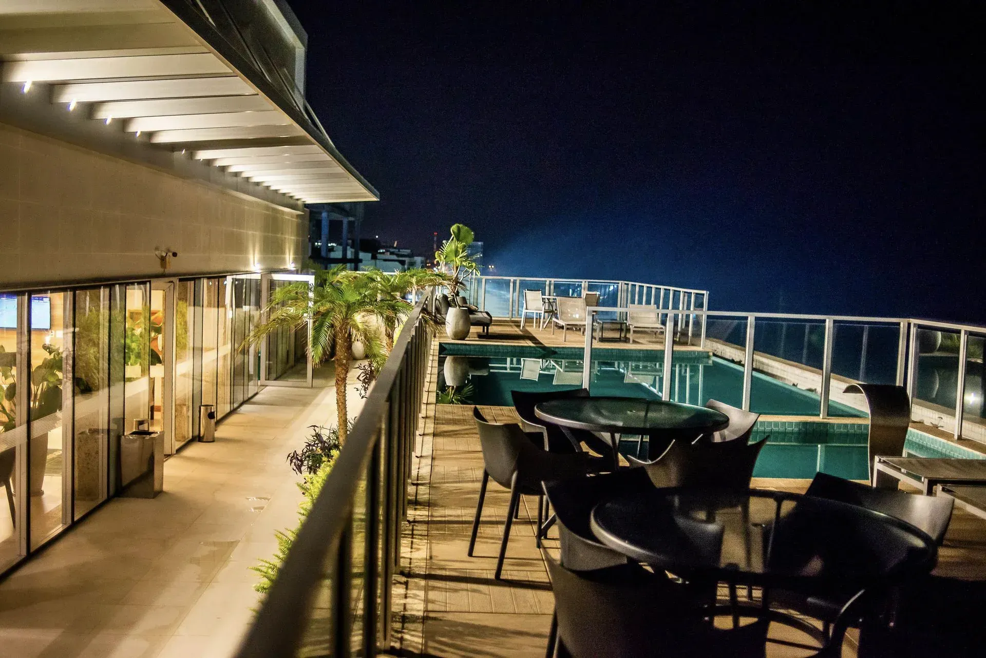 Restaurante com terraço na cobertura, aberto à noite, com mesas, cadeiras e vista para o mar sob luzes aconchegantes.