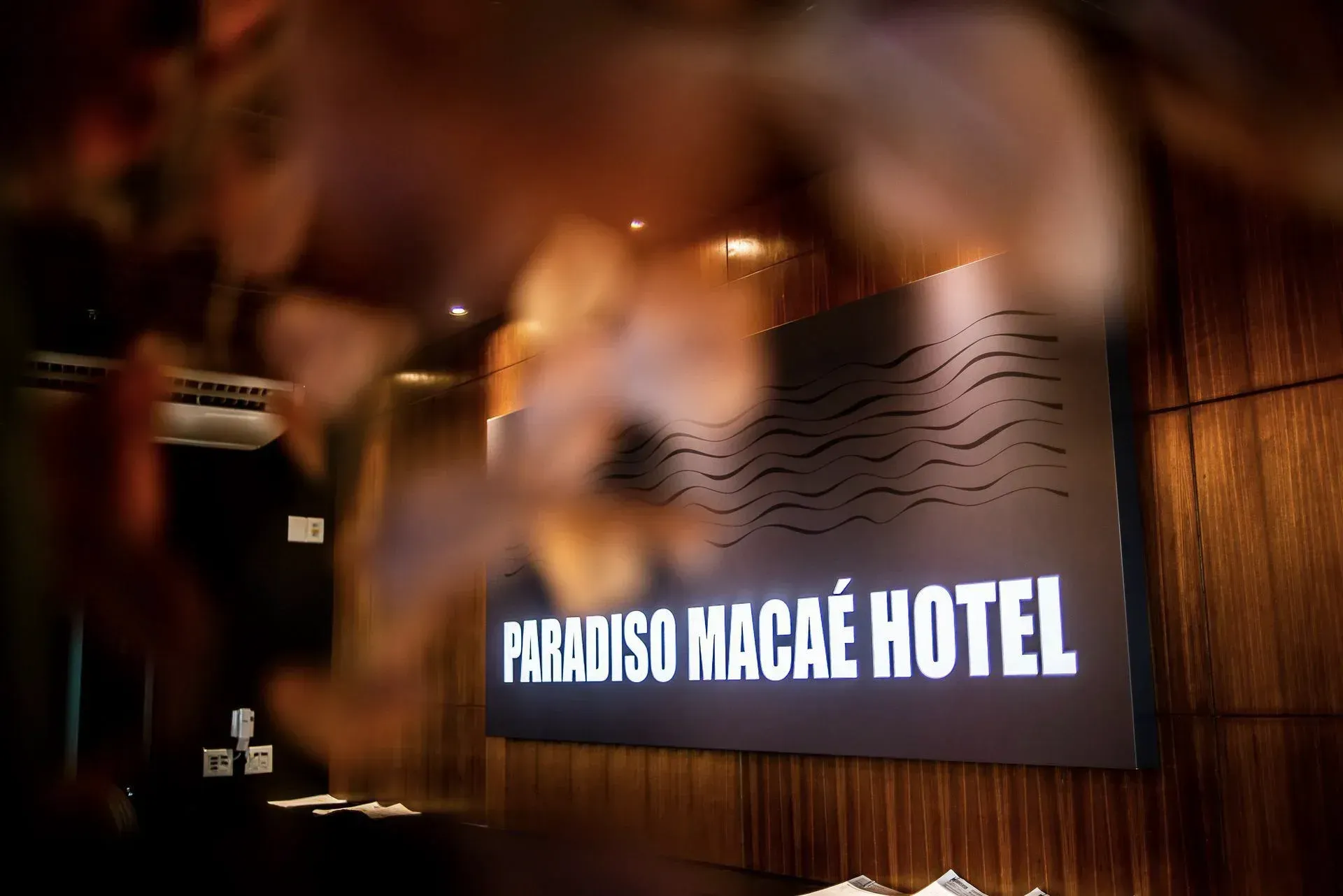 Placa com os dizeres “HOTEL PARADISO NAÇÃO” em uma parede escura com iluminação aconchegante.