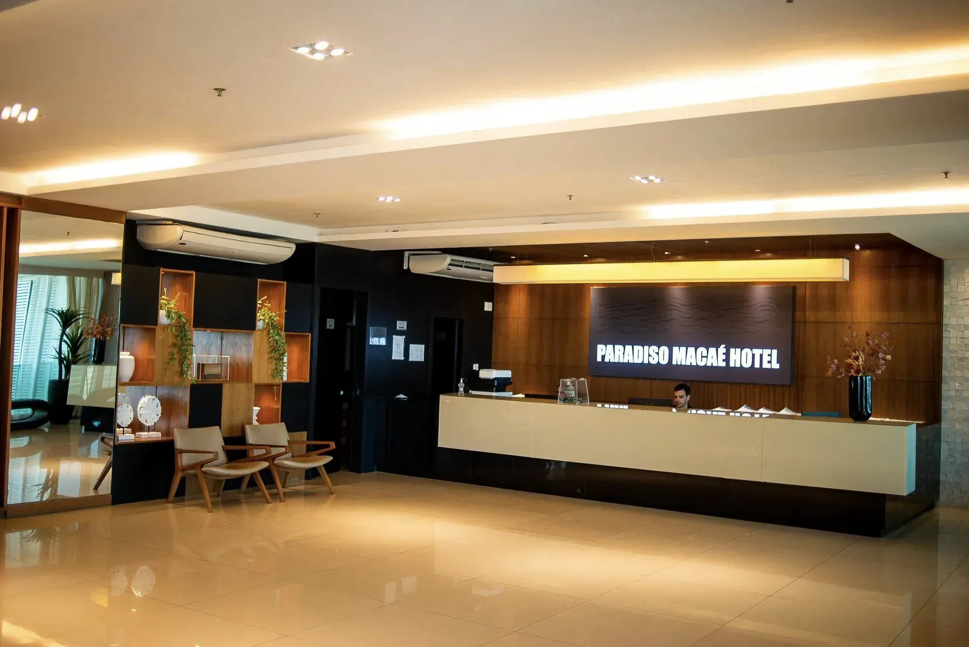 Hall de entrada moderno do hotel com balcão de recepção, iluminação aconchegante e piso polido.