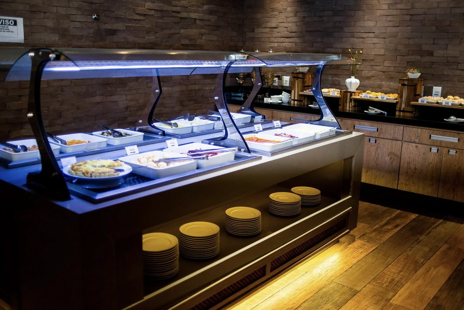 Buffet moderno com pratos e travessas cobertos sobre uma bancada de madeira em um restaurante com pouca luz.