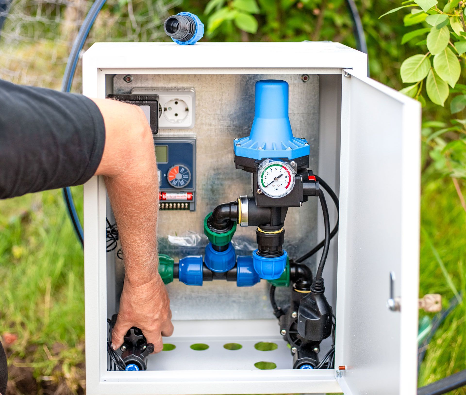 Open electrical control box with blue water filtration equipment and a hand adjusting a valve