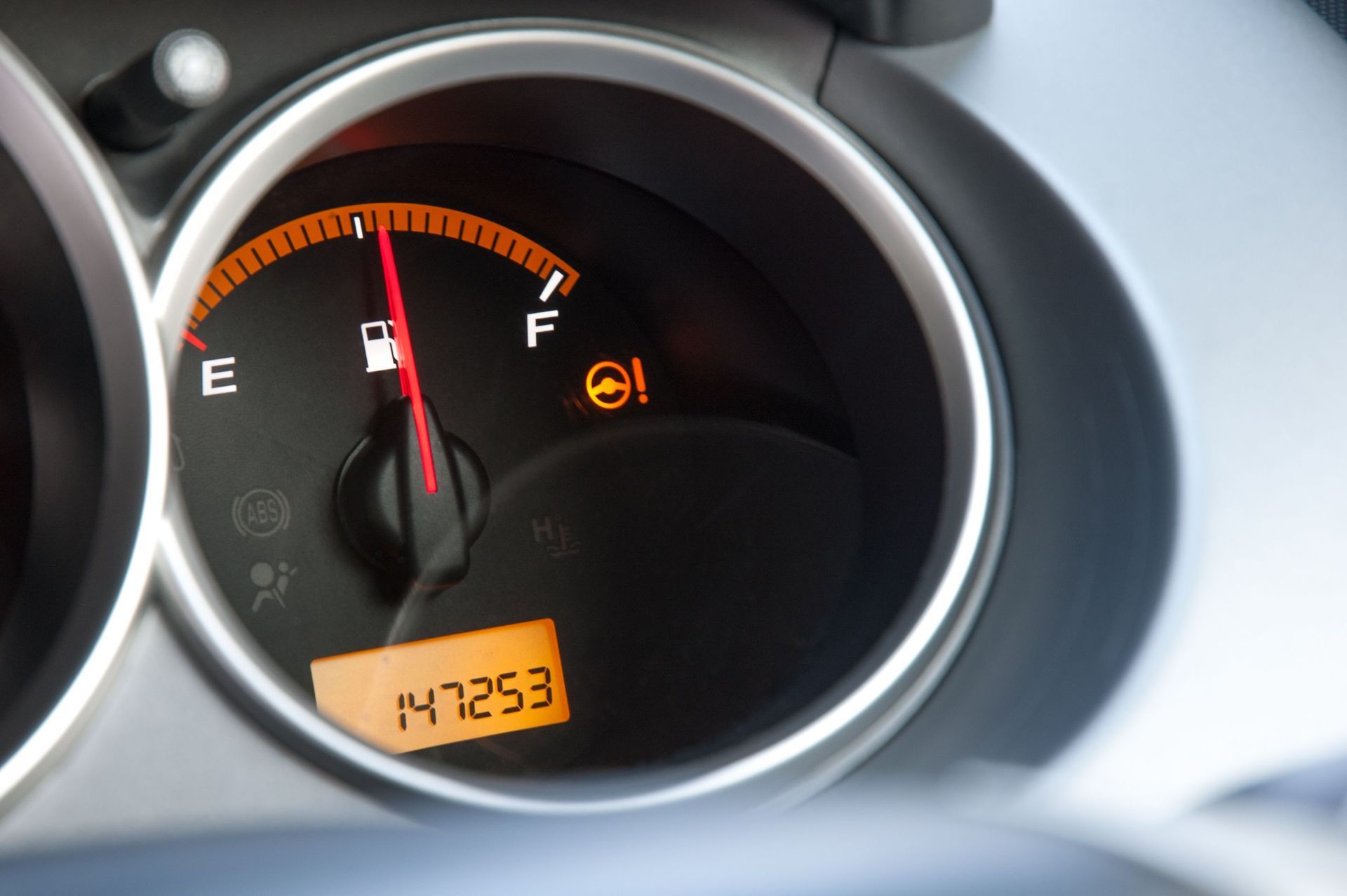 Car dashboard fuel gauge near empty with low-fuel warning light and odometer reading 147263