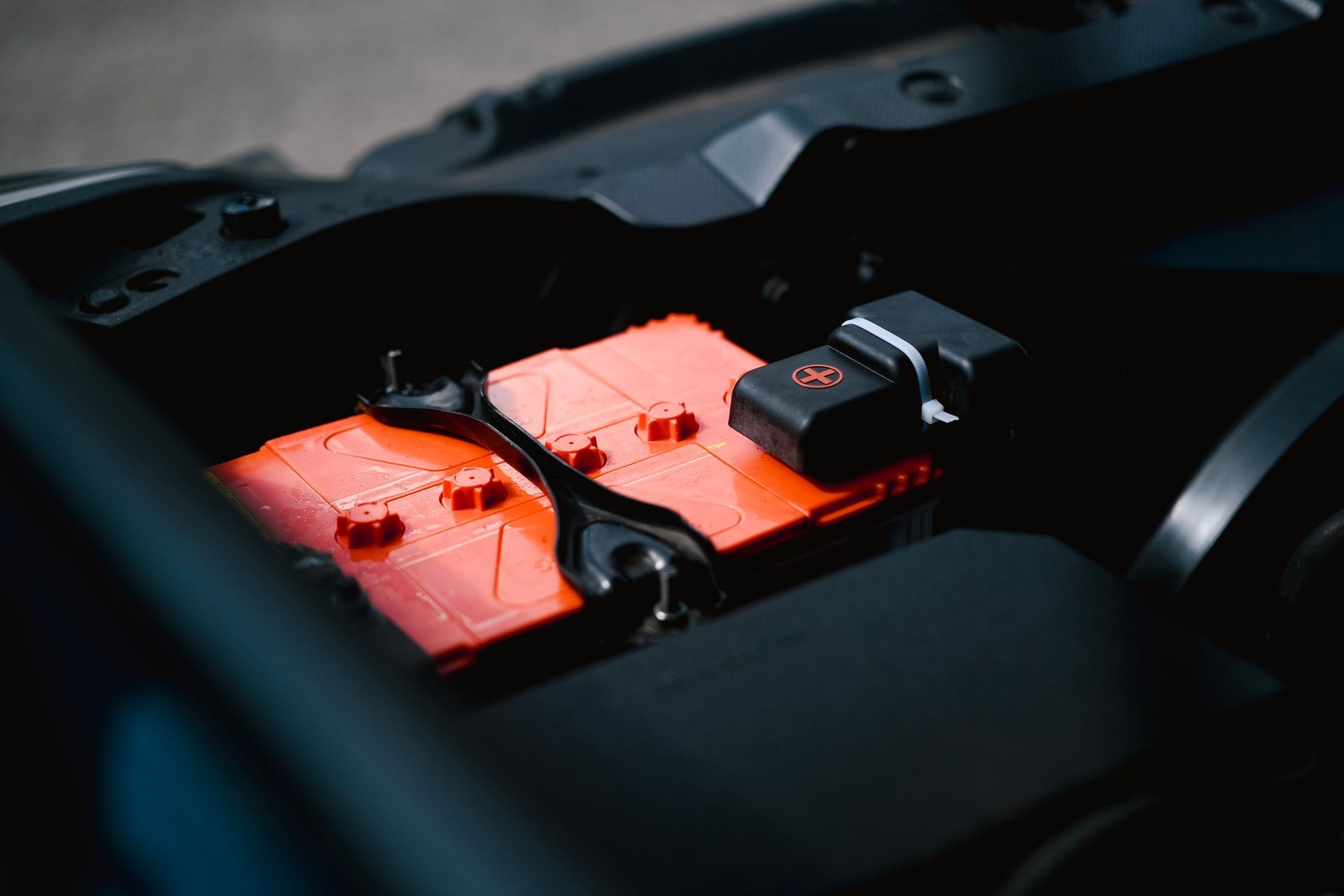 Red car battery in a dark engine bay with red battery covers