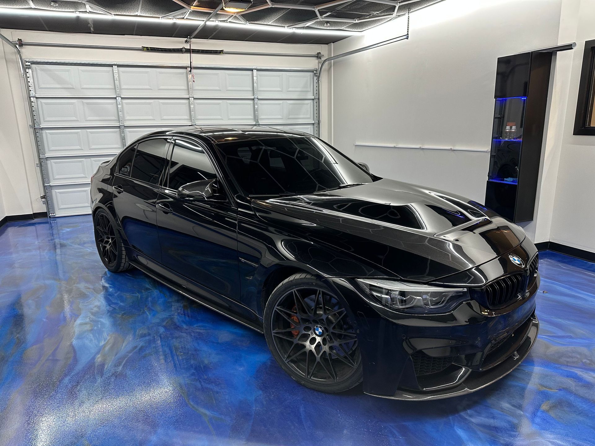 Black hatchback parked in a garage with a blue floor and white walls