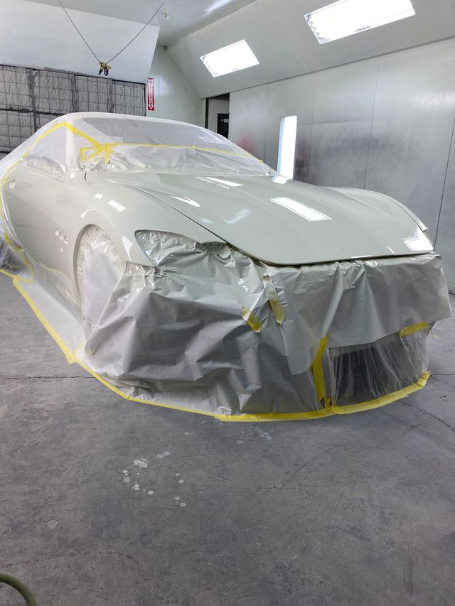White car wrapped in protective plastic and masking tape inside a paint booth