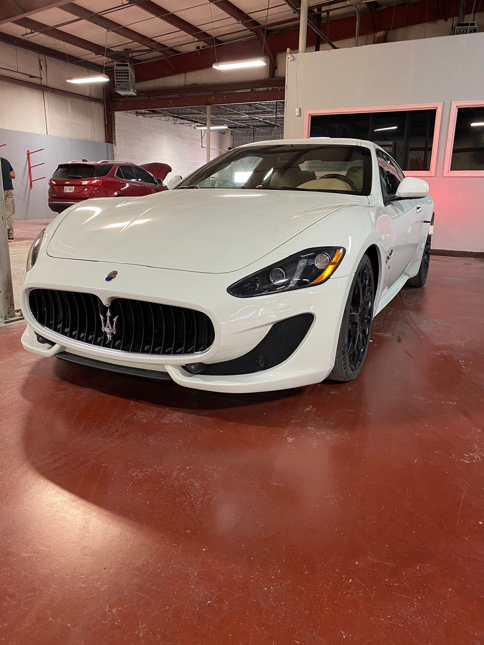 White sports car in a showroom, angled front view on a red floor with other cars in the background