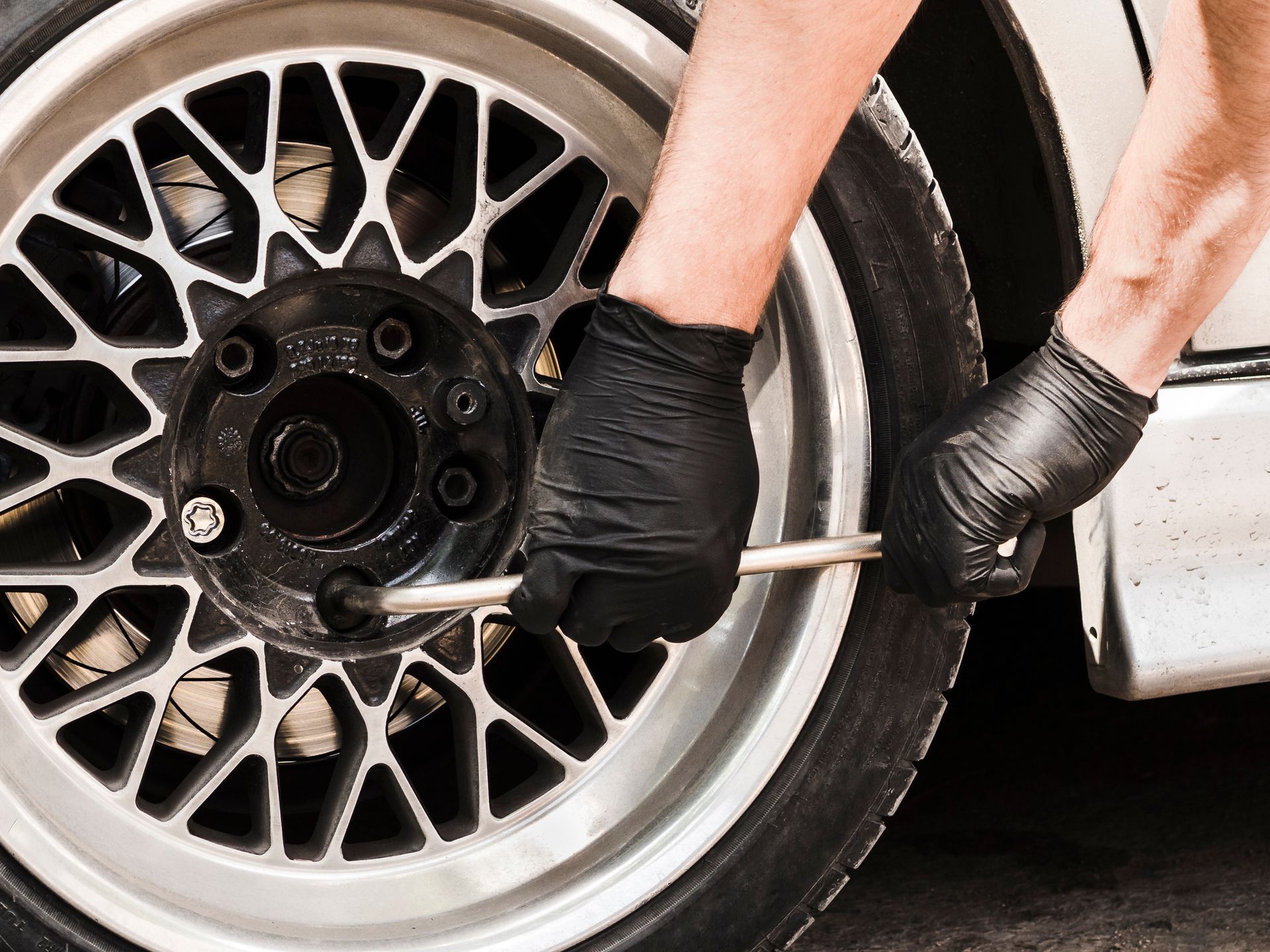 Close-up of an orange classic car’s wheel with chrome rim and white-letter tire on wet pavement