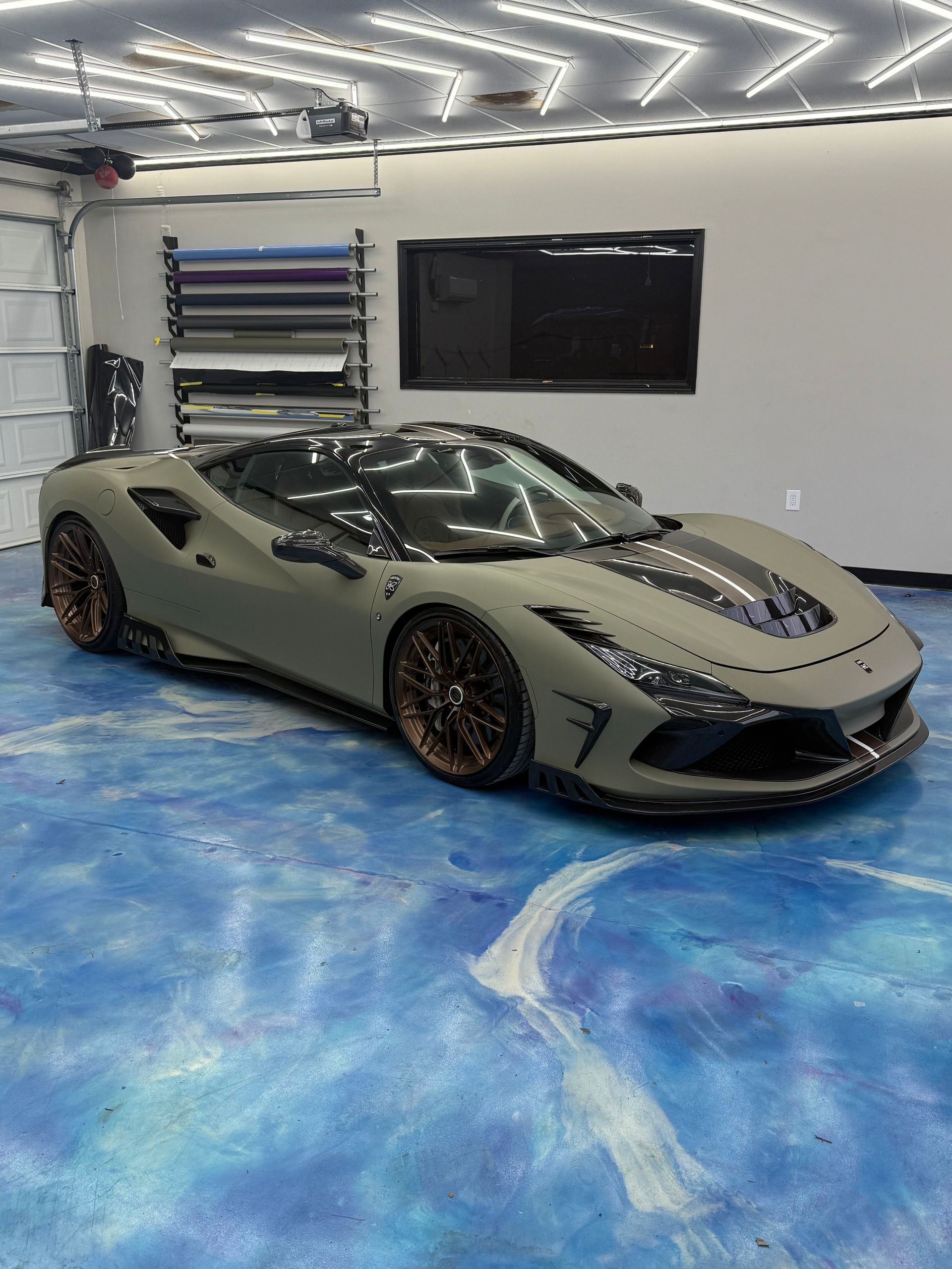 Gray supercar parked in a garage with bright overhead lights and a blue epoxy floor