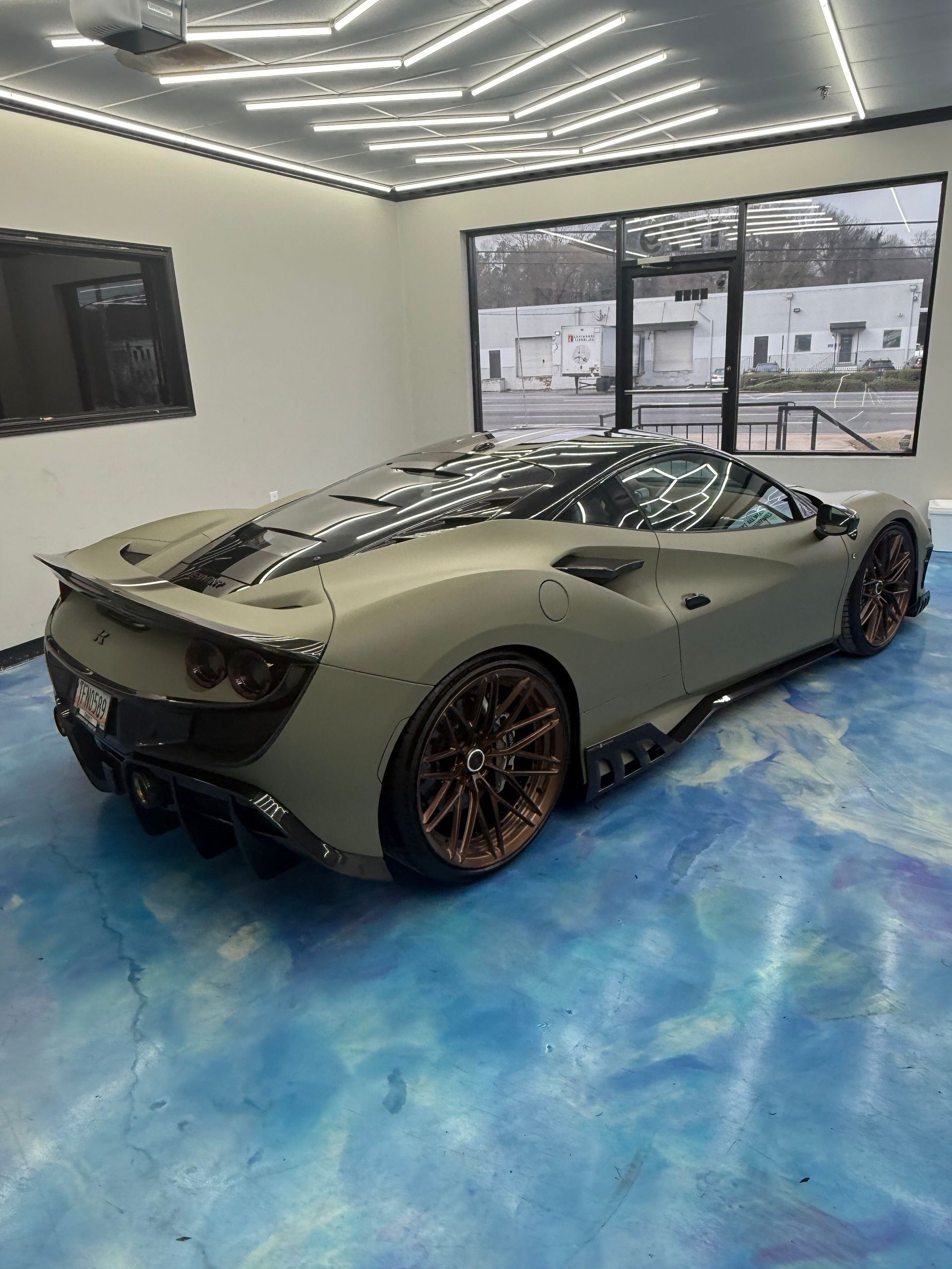 Matte green sports car in a showroom with blue floor and large glass windows
