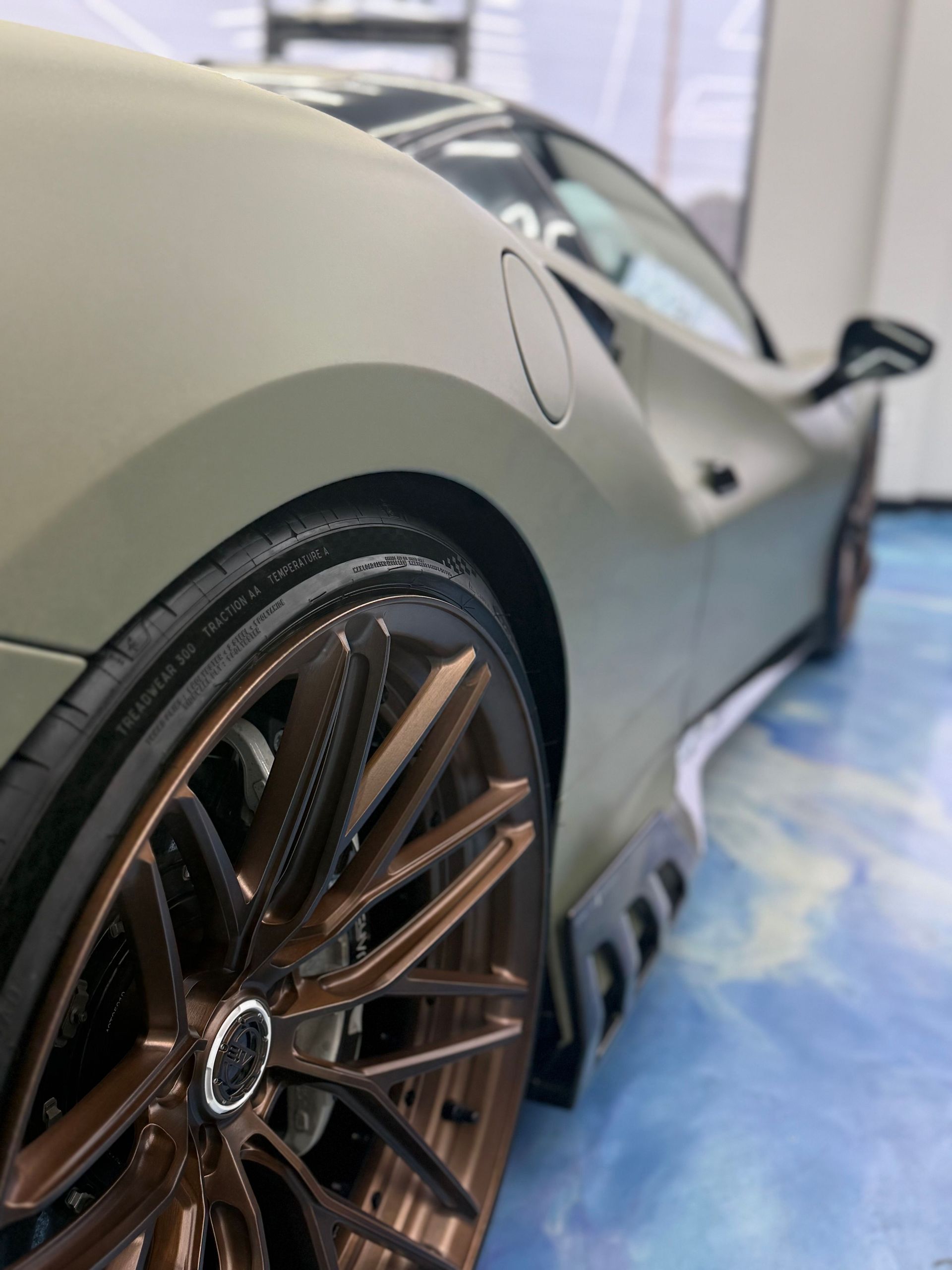Close-up of a matte gray sports car’s rear wheel and fender in a showroom