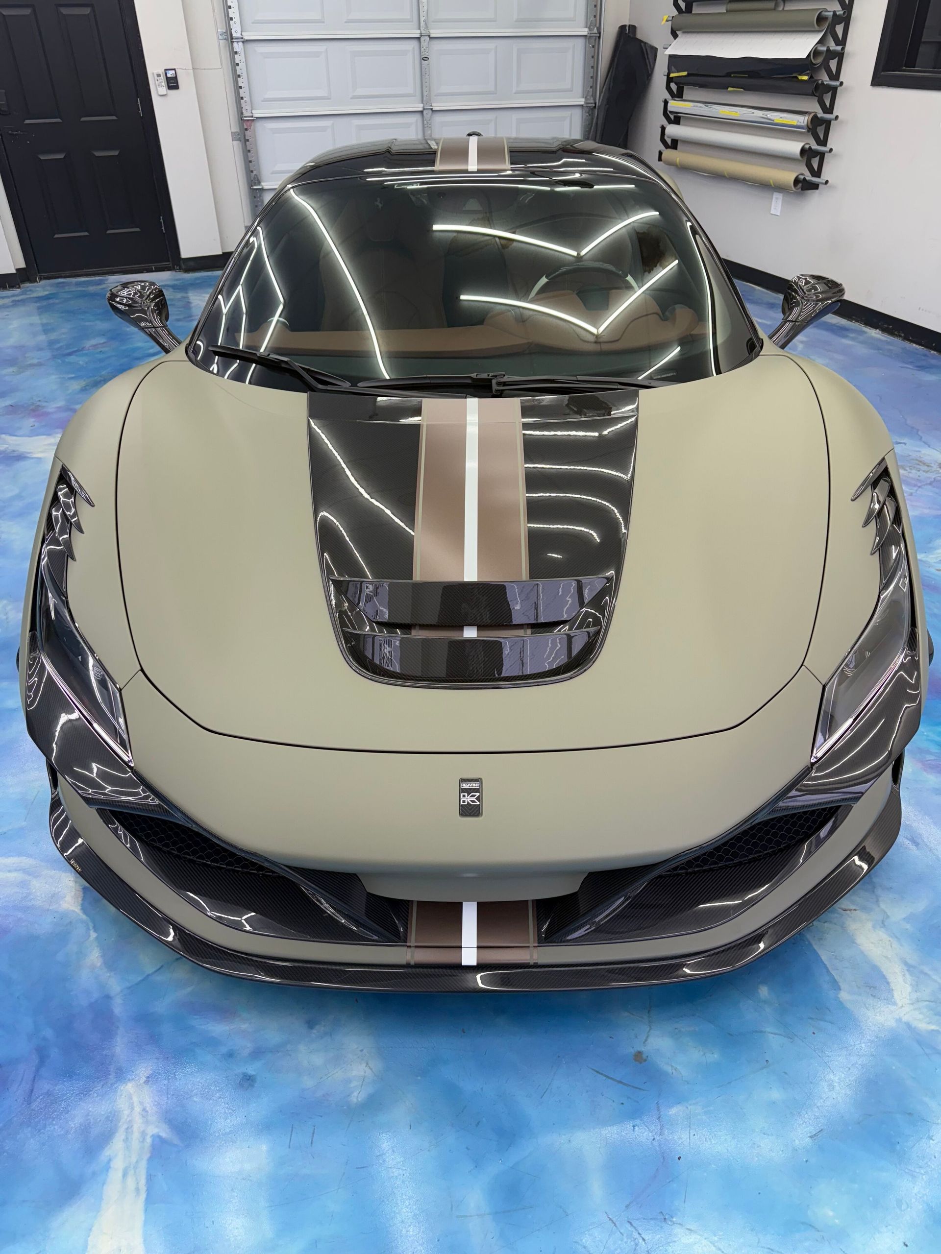 Front view of a beige sports car with black and gold racing stripes in a garage.
