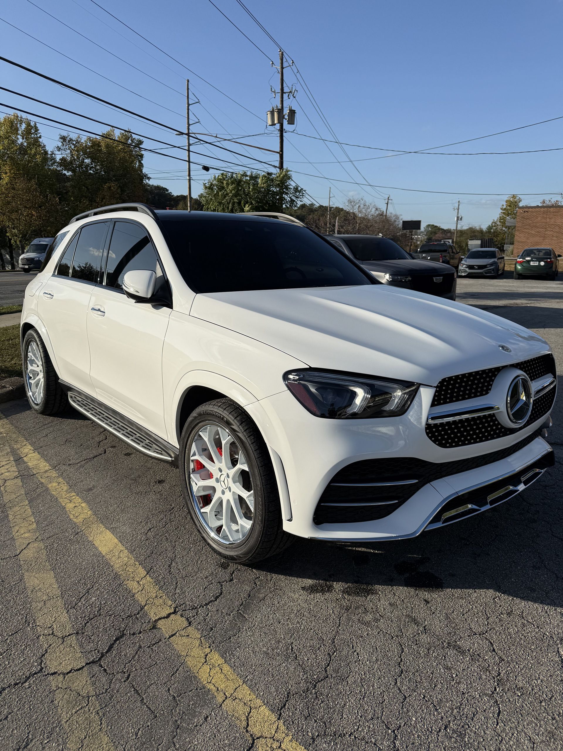 White Mercedes SUV parked in a lot under a clear blue sky, front three-quarter view.