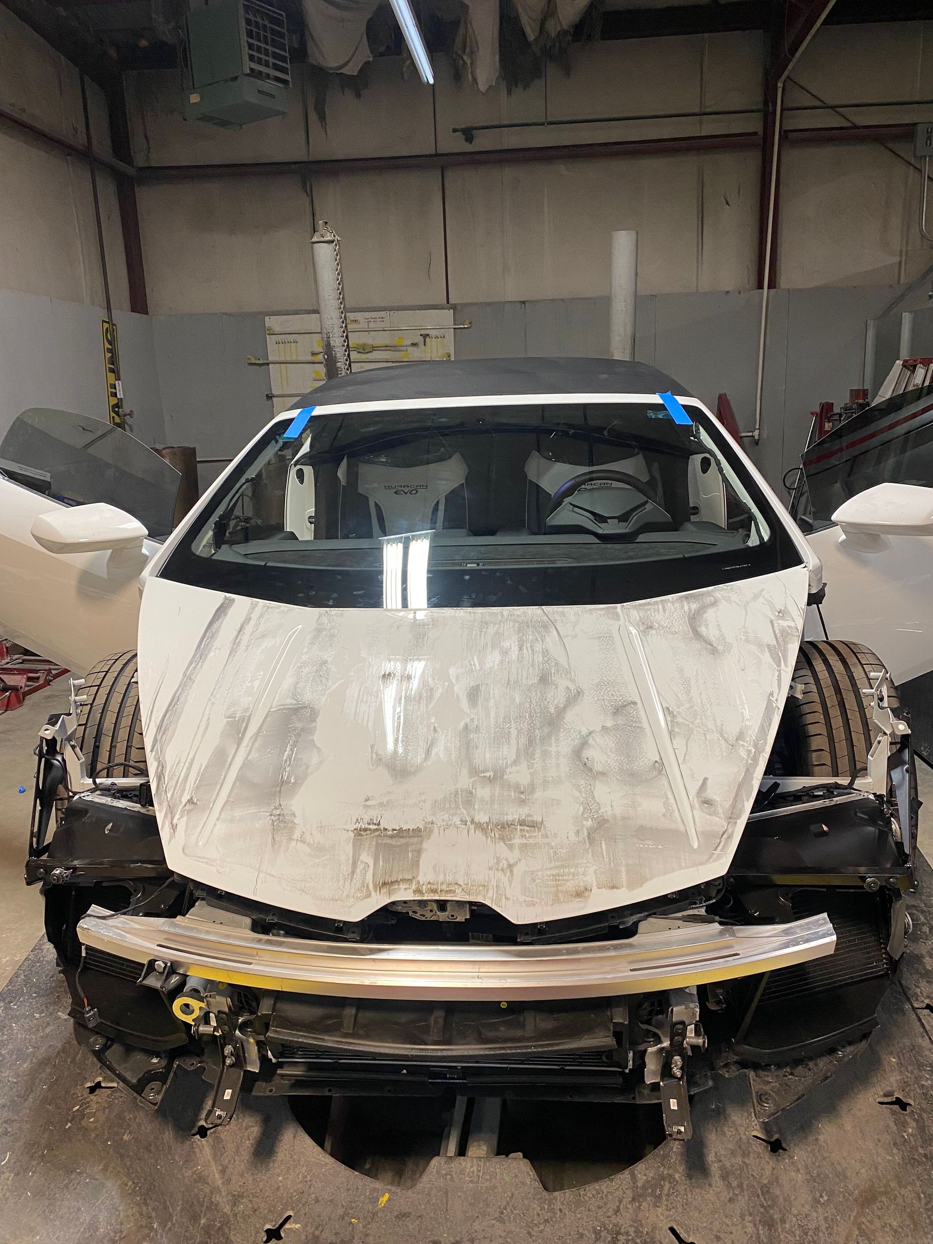 Damaged white car front end in a garage, with bumper and headlights removed