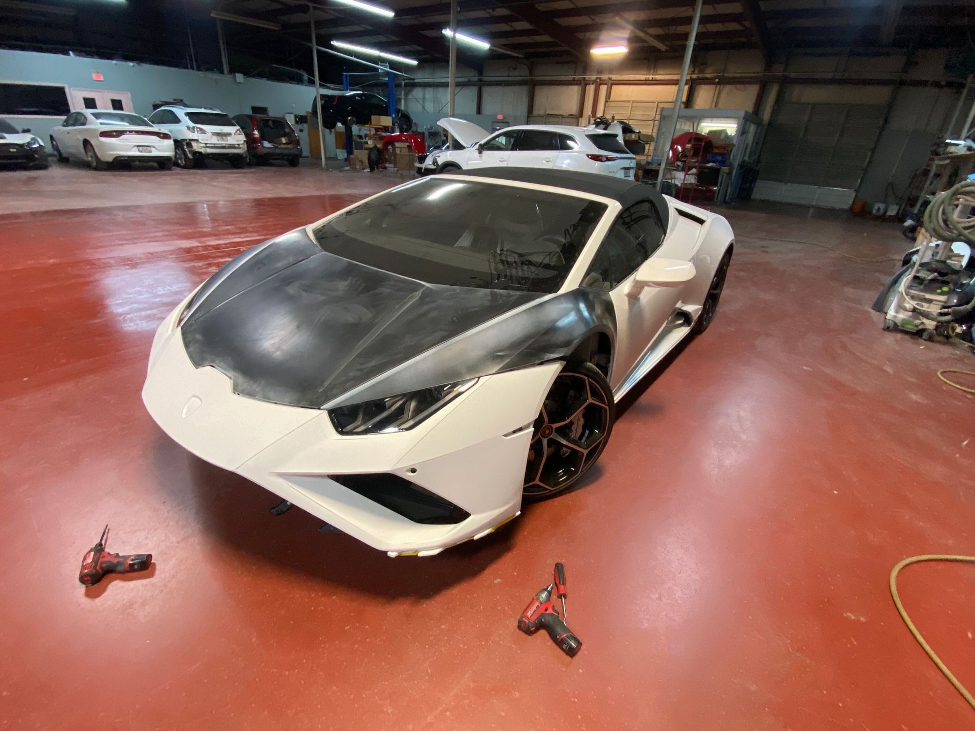 White sports car in a garage with tools on the floor and other cars in the background