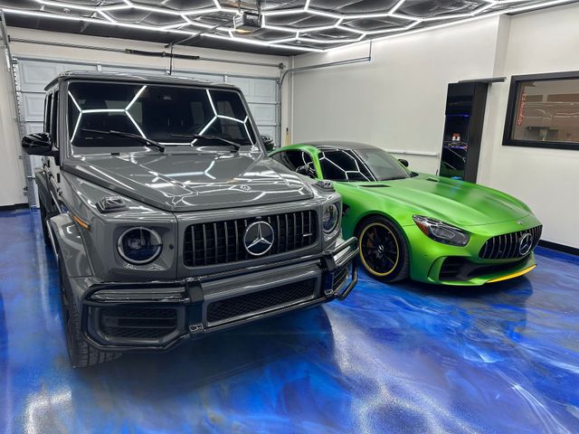 Two luxury cars in a modern garage: a gray SUV and a bright green sports coupe on a blue floor.