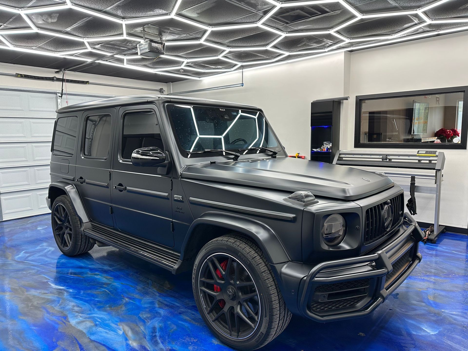 Black Mercedes G-Class SUV in a modern garage with blue floor and geometric ceiling lights
