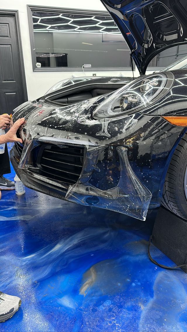 Car wrapped in clear protective film being applied in an auto detailing shop