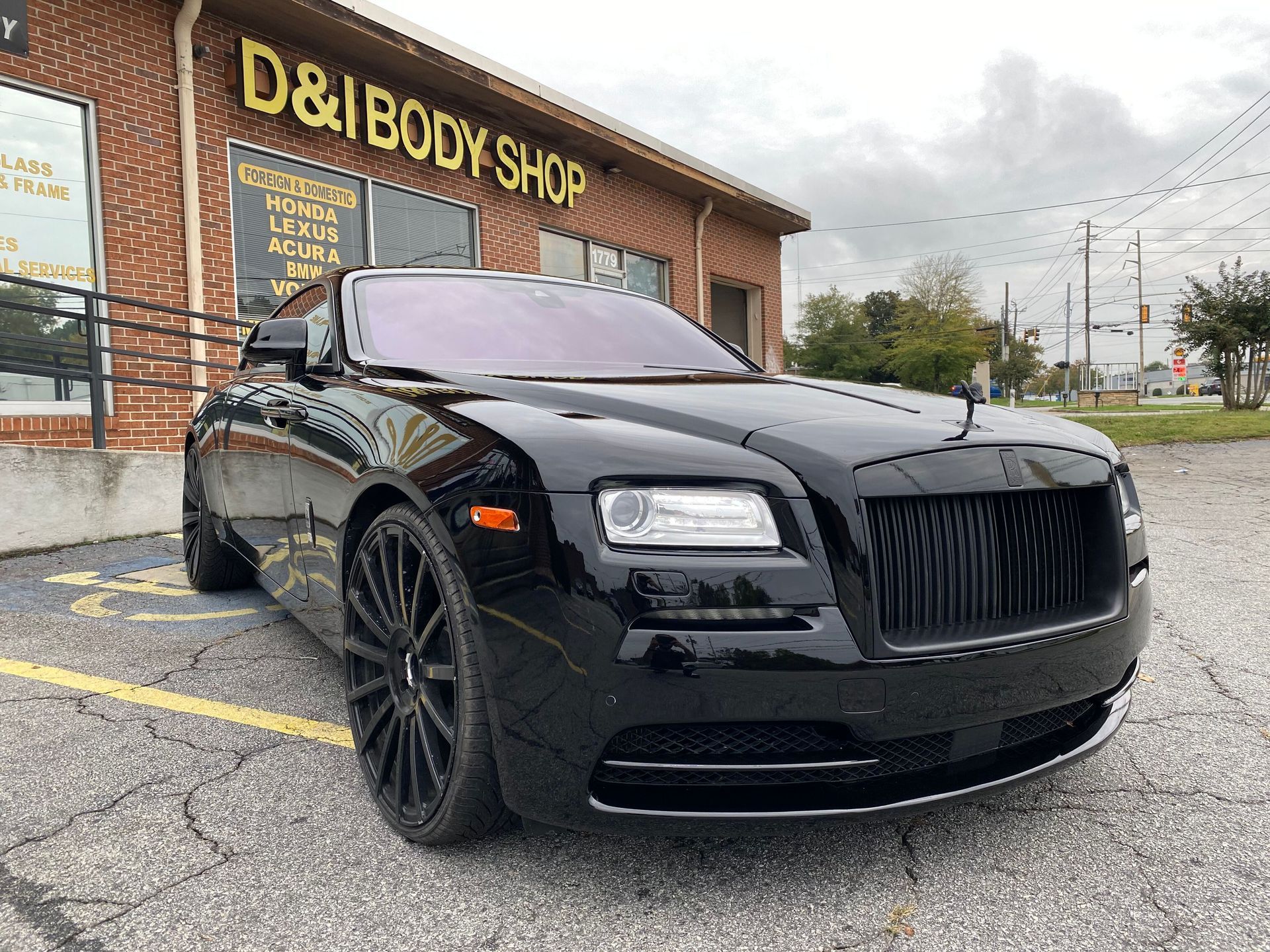 Black Rolls-Royce parked outside a D&I body shop on a wet day