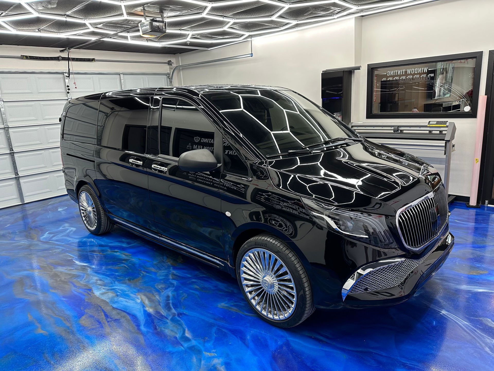 Black luxury van in a modern garage with a blue floor and geometric ceiling lights