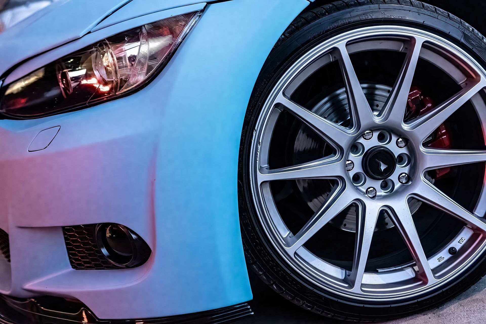 Close-up of an orange classic car’s wheel with chrome rim and white-letter tire on wet pavement