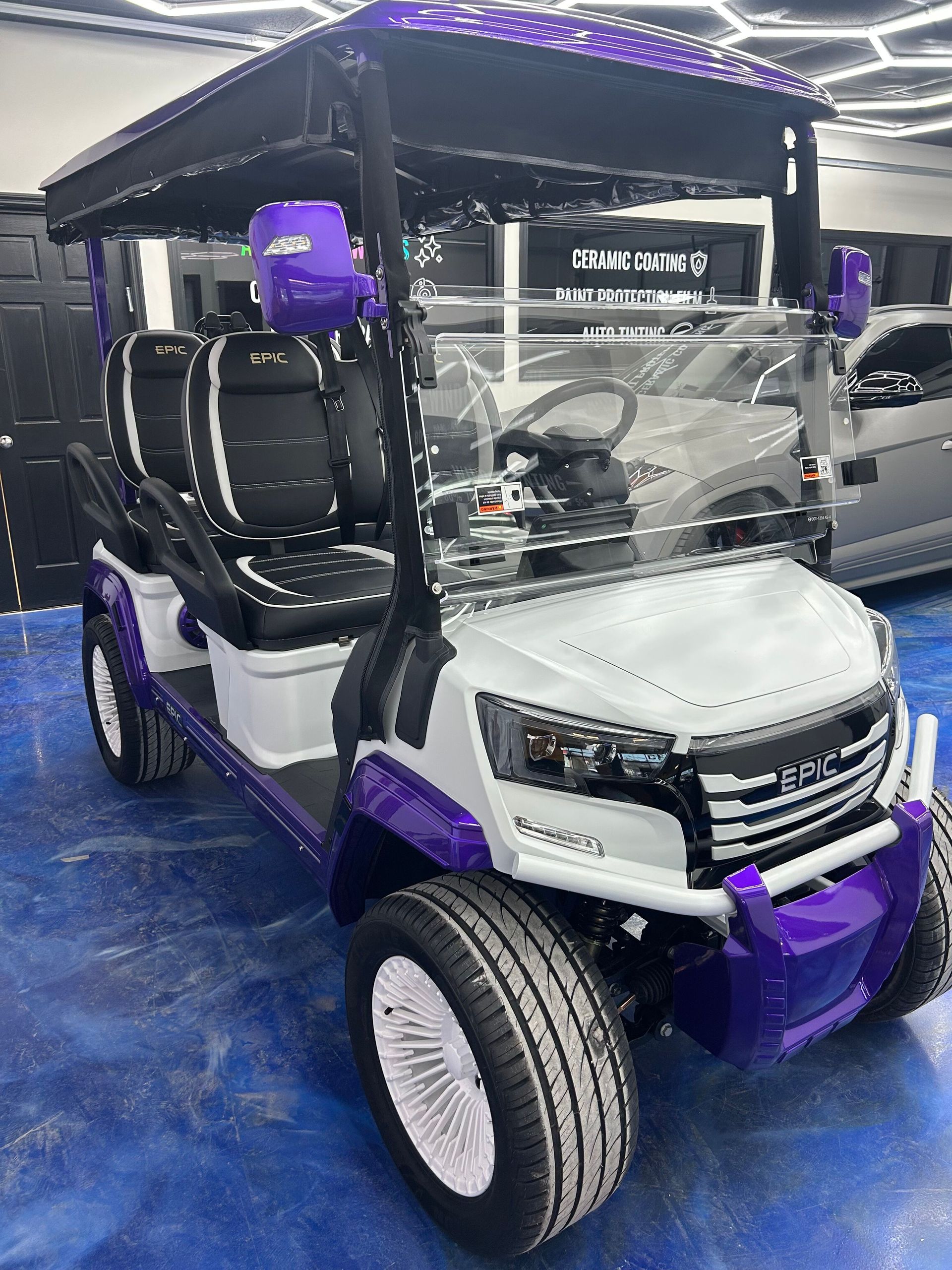 Purple-and-white golf cart with roof and windshield on a blue floor at an indoor expo