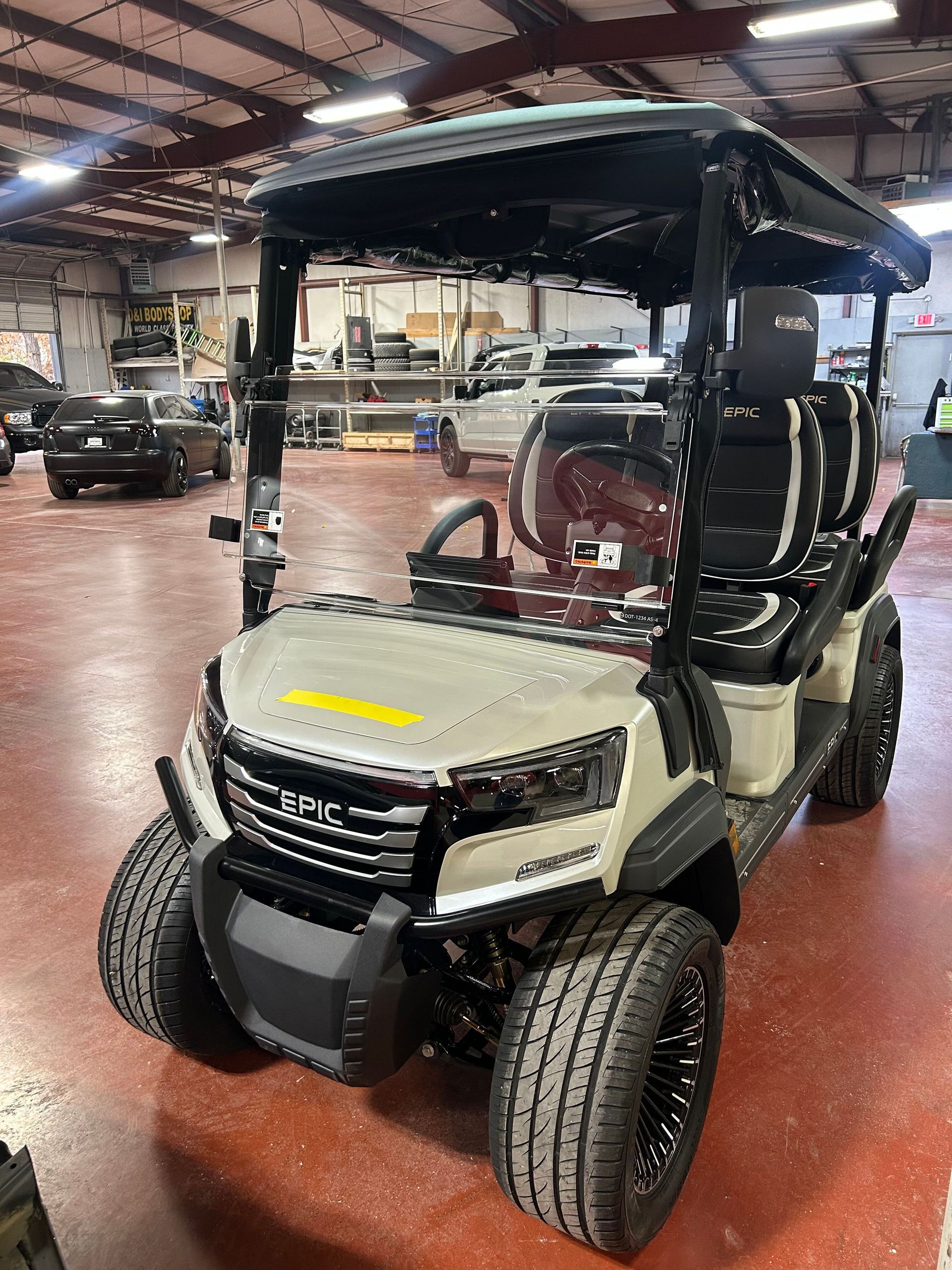 Golf cart with black canopy and beige body parked inside a warehouse garage.