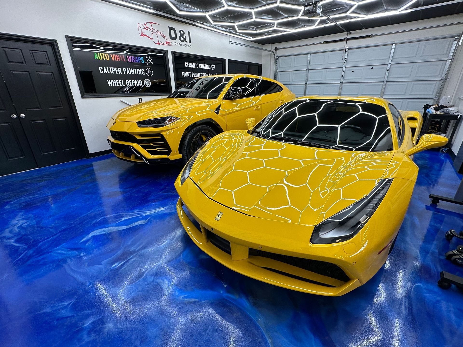 Two yellow sports cars parked in a modern garage with a glossy blue floor and geometric ceiling lights