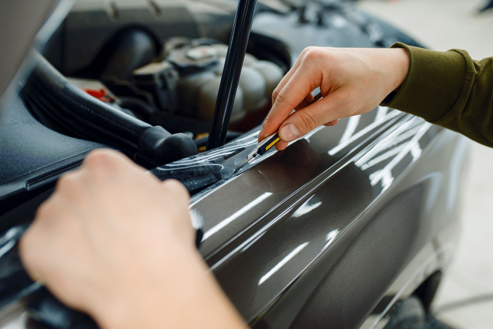 Hands applying vinyl wrap to a glossy black car hood with a squeegee tool