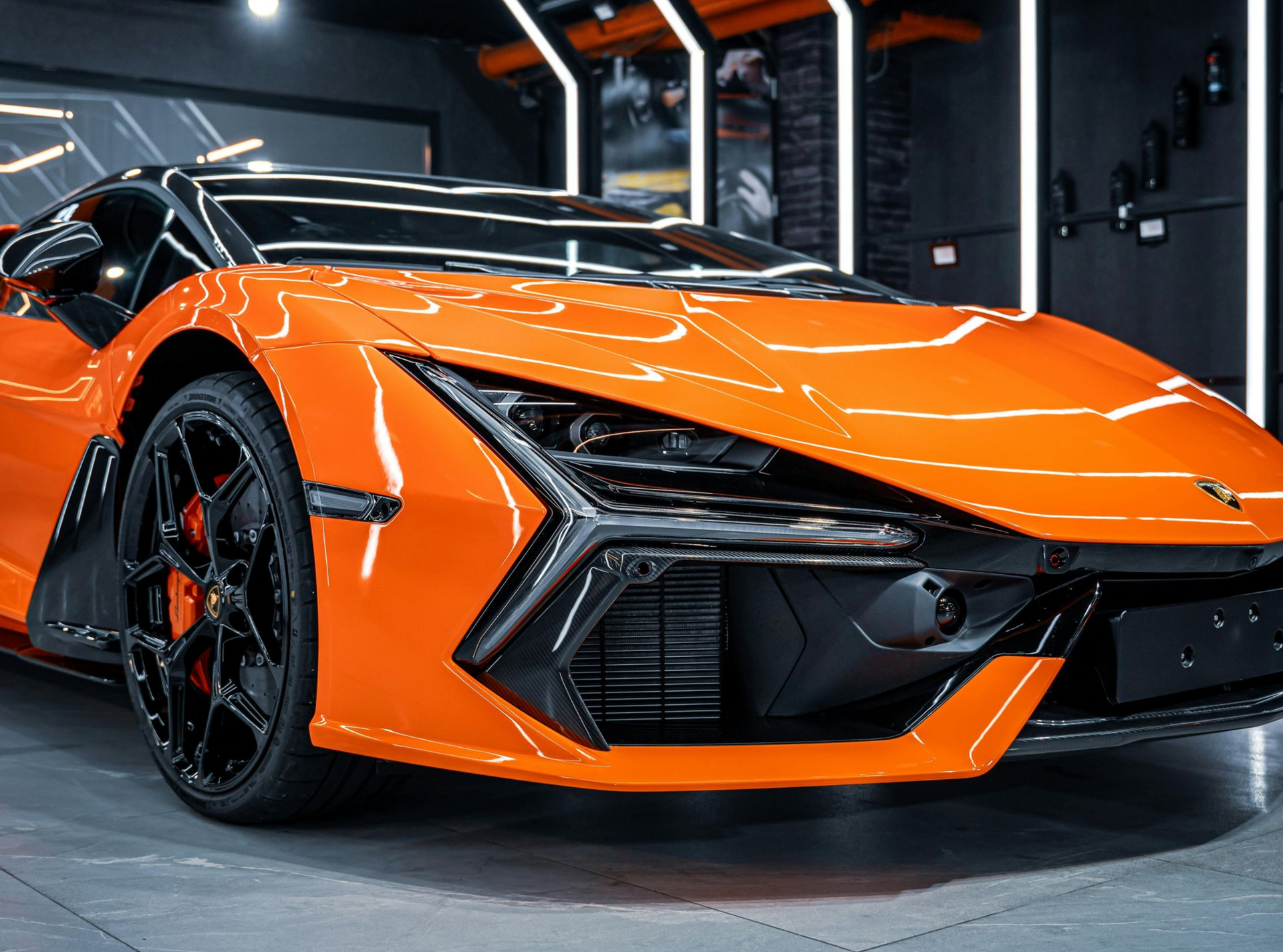 Orange sports car in a garage, viewed from the front with black accents and glossy finish